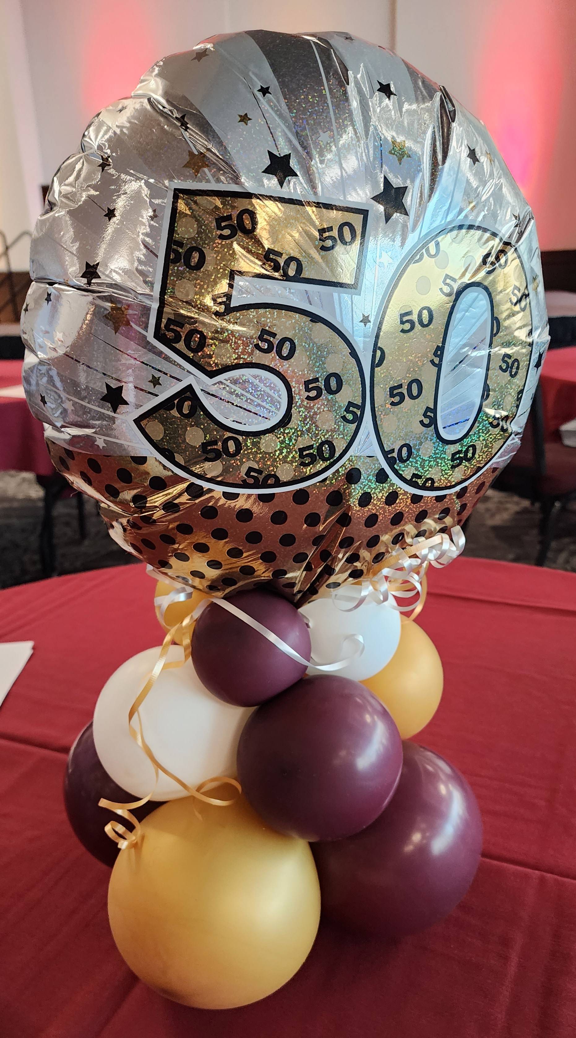 An arrangement of maroon, gold, and white balloons topped by a bigger balloon with the number 50 on it.