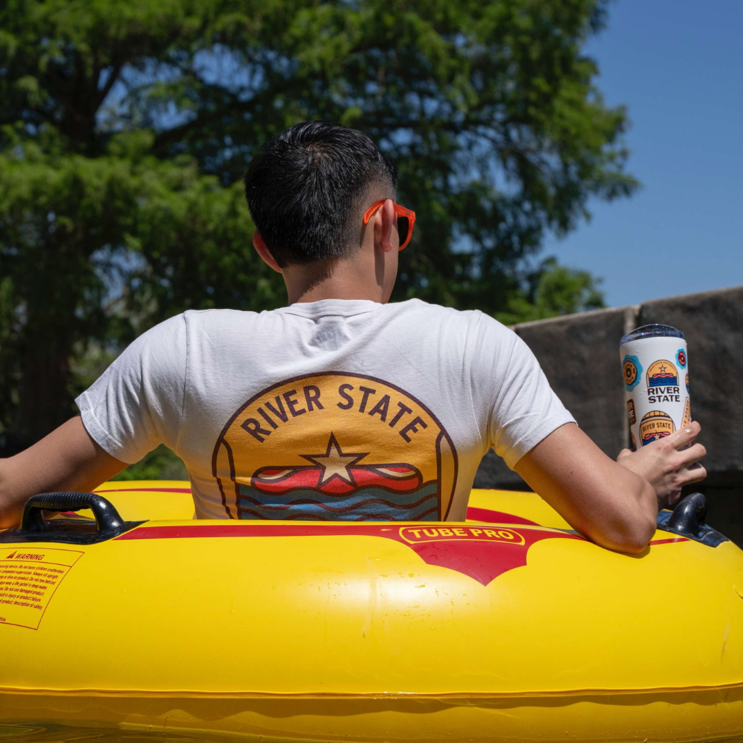 image of a student in a River State shirt by TXST on the San Marcos River in a floating tube