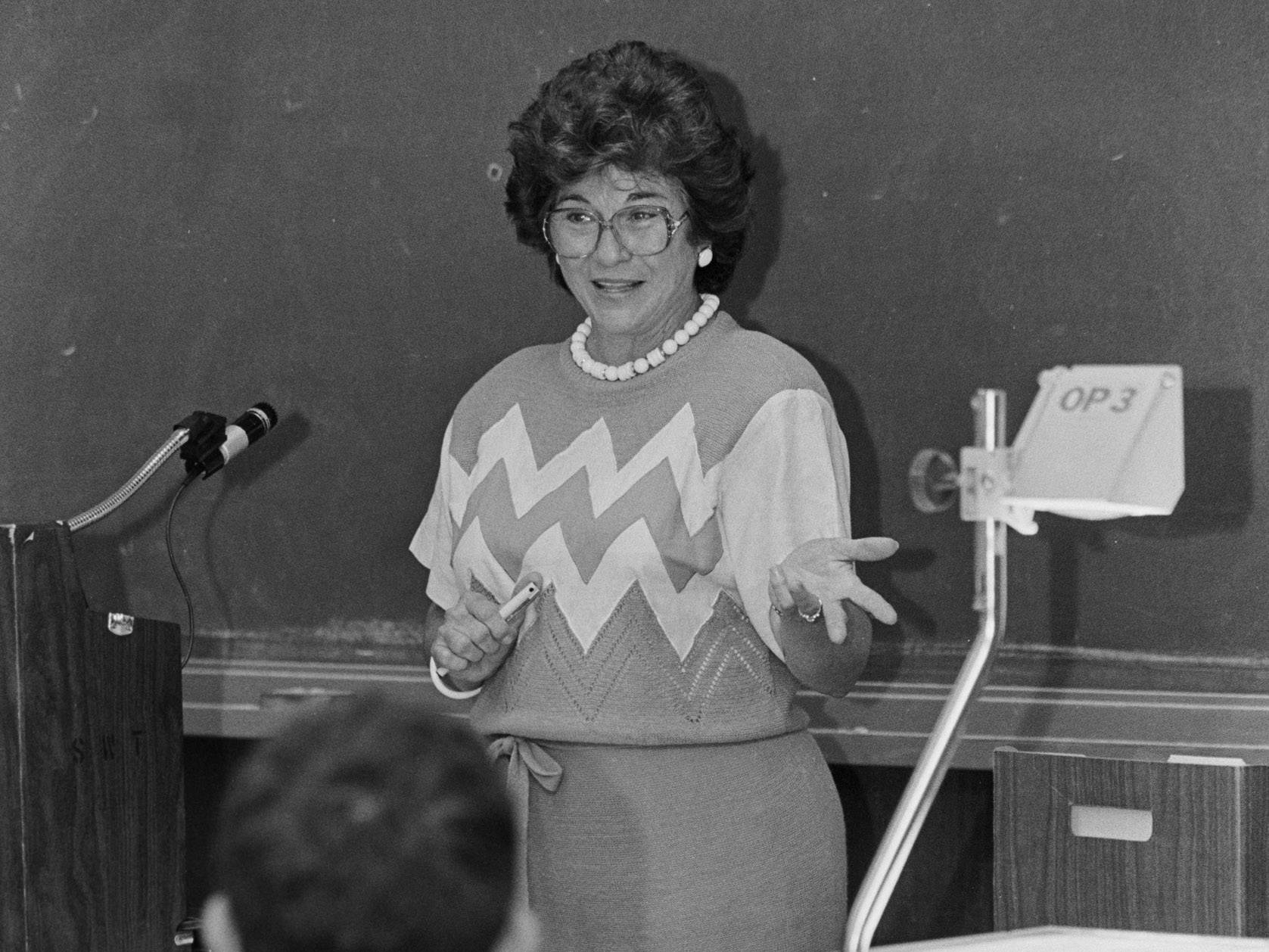 black and white photo of woman teaching in front of chalk board