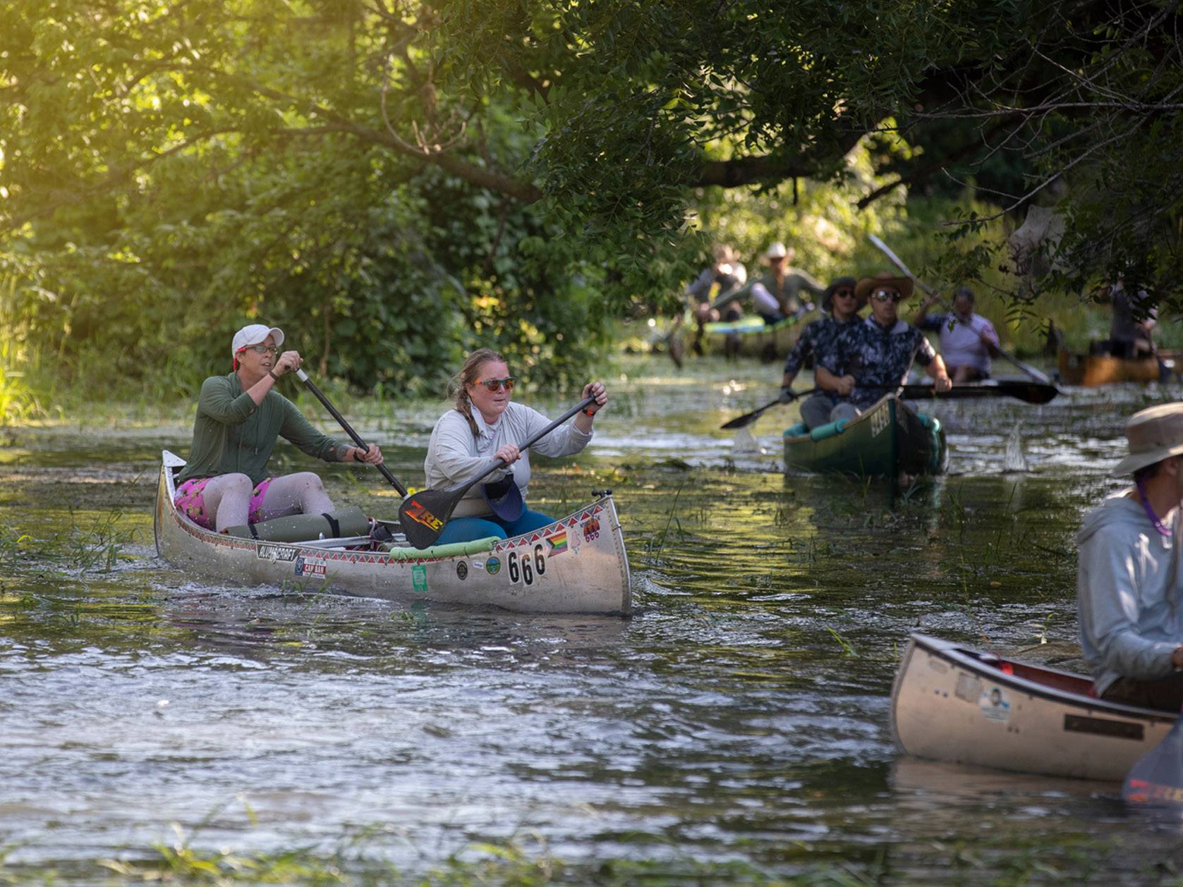 people in multiple canoes on river