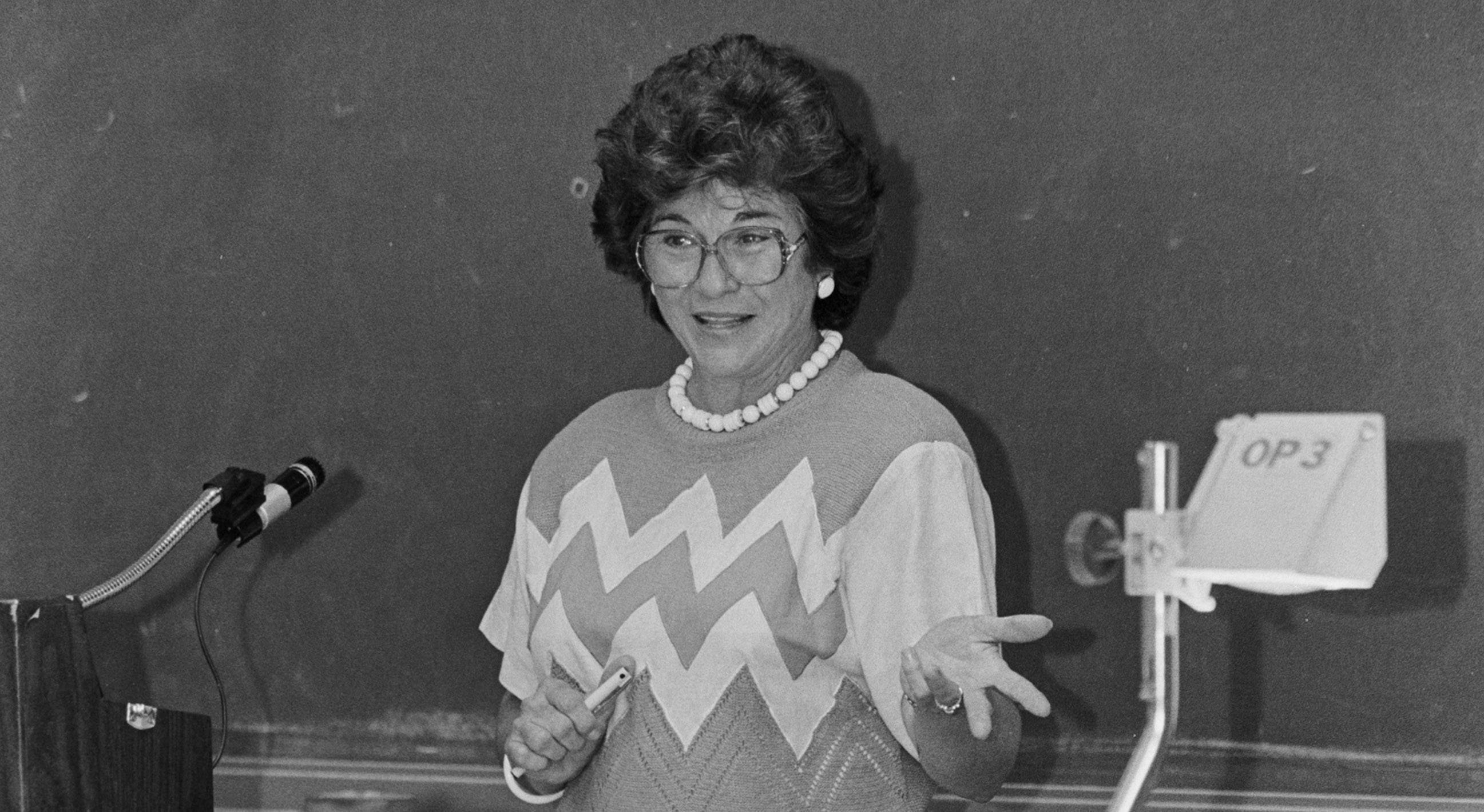 black and white photo of woman teaching in front of chalk board