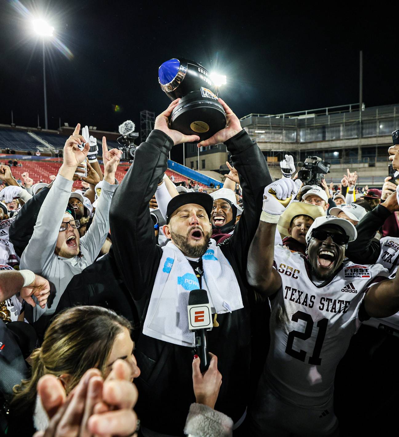 football coach holding up trophy in middle of group of football players