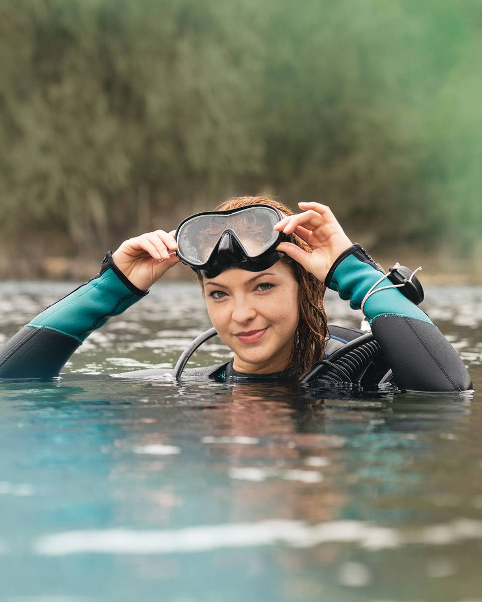 woman in water holding goggles on top of head
