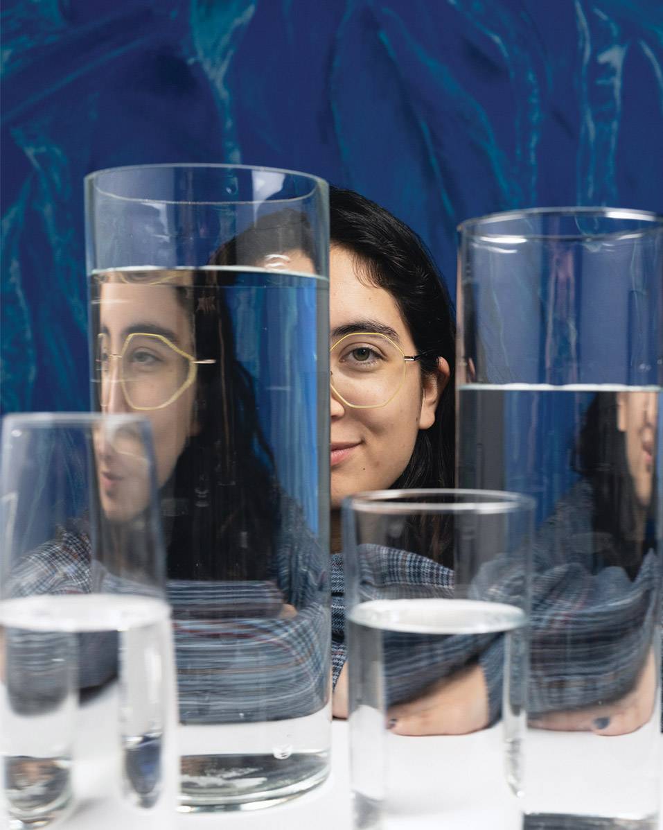 womans face behind multiple glass canisters filled with water