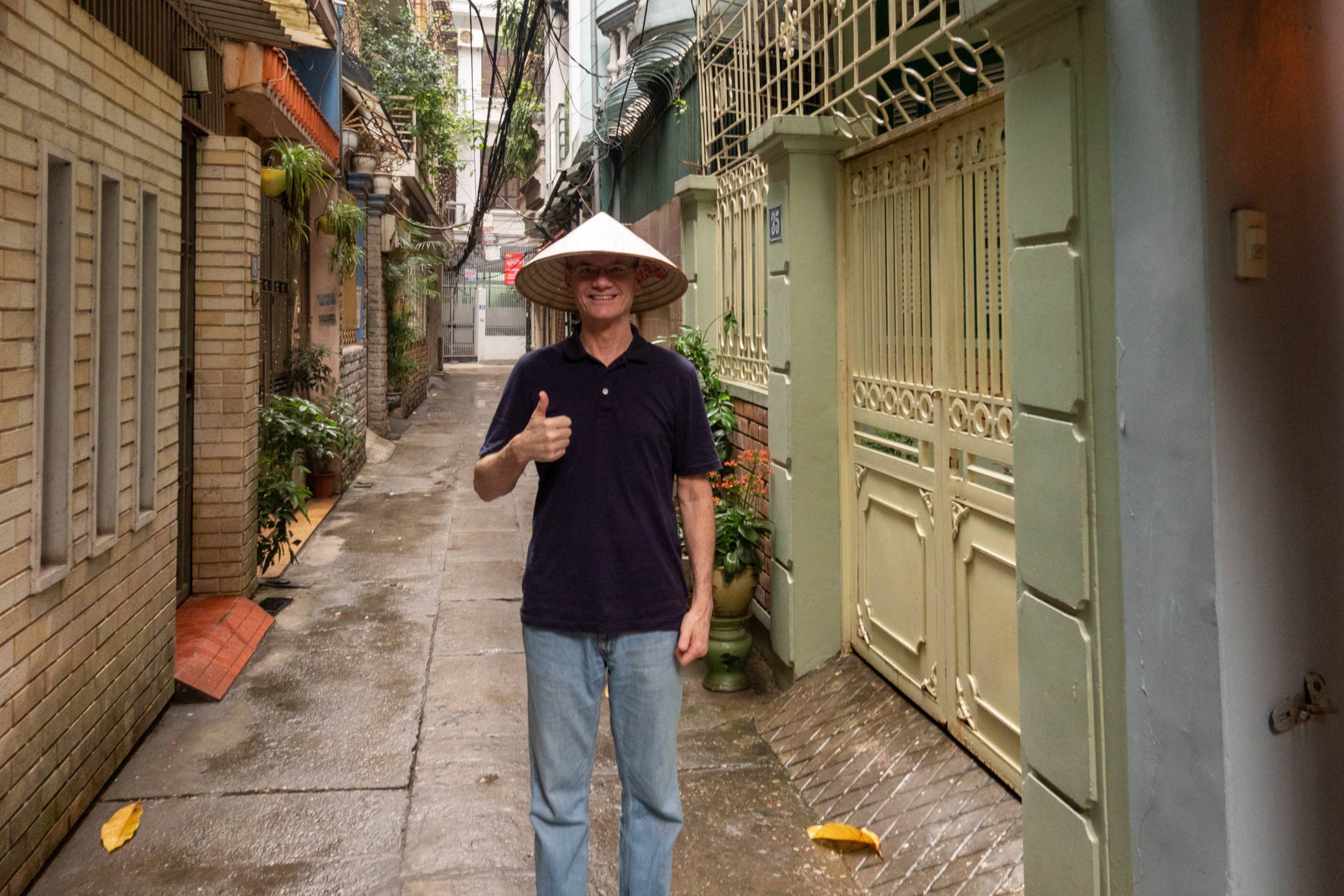 Picture of me wearing a Vietnamese cone hat standing in an alleyway. 