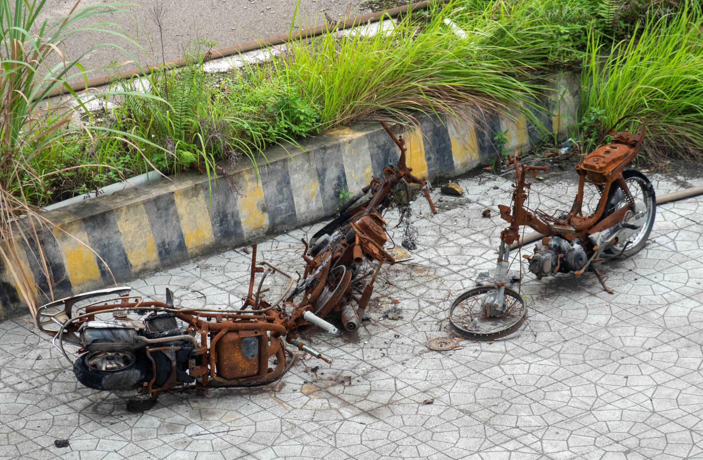 Picture of three rusted motorbikes that look like they might have been set on fire and left to rust
