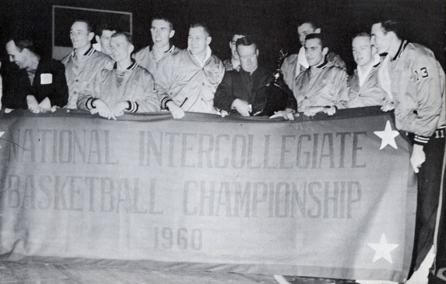 Members of the 1960 TXST men’s basketball team pose for a photo while holding a championship banner. The young men are all smiling in celebration of the their success while wearing matching uniforms.