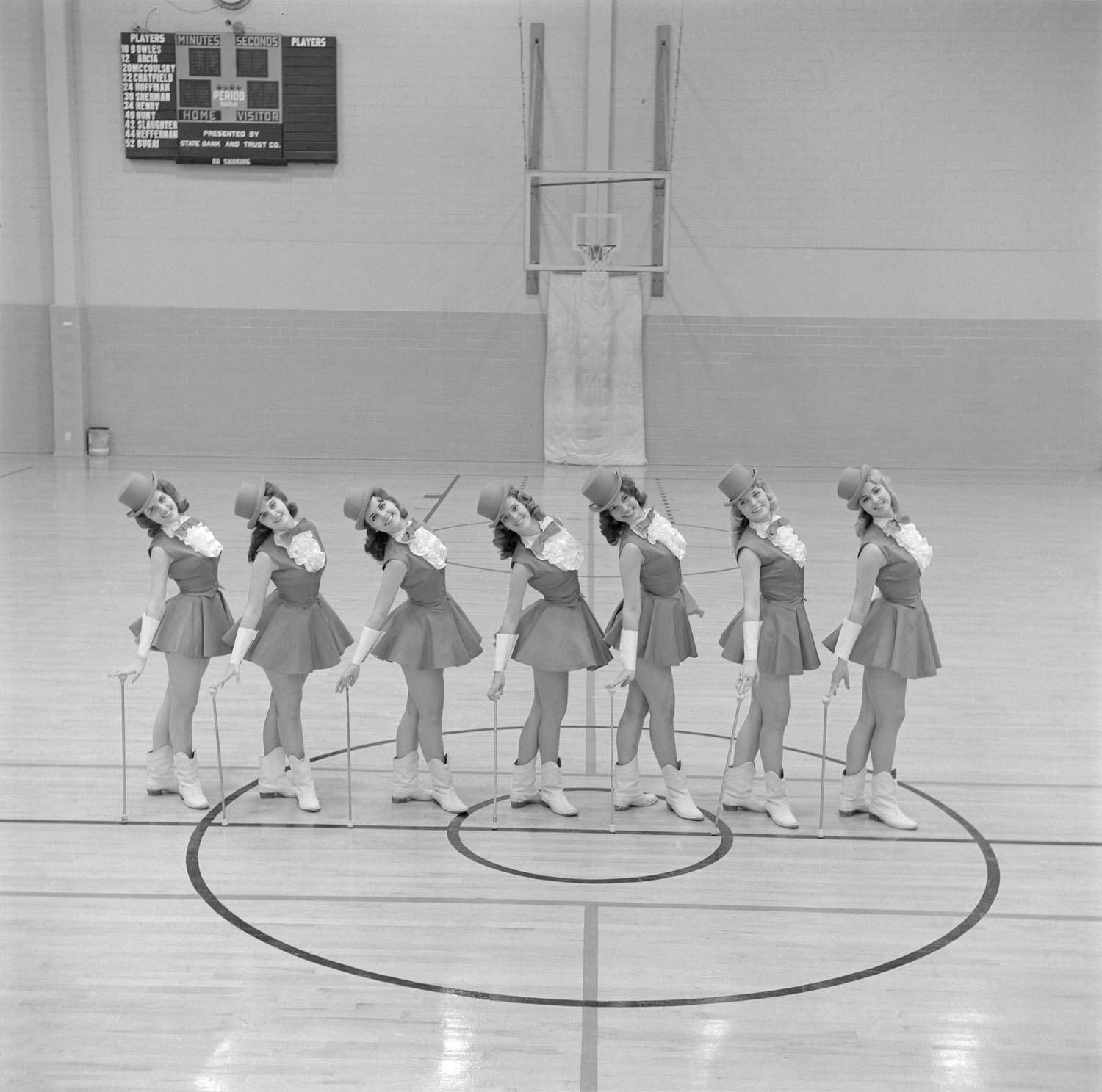 Seven Strutters gather in Jowers, posing with arched backs as they hold dancing canes. 