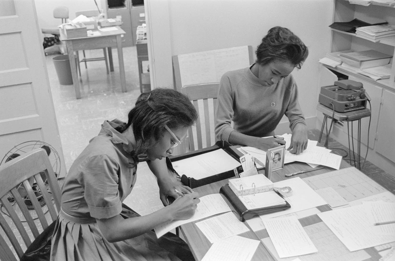 Two of the First Five are signing forms at a table filled with registration documents. 