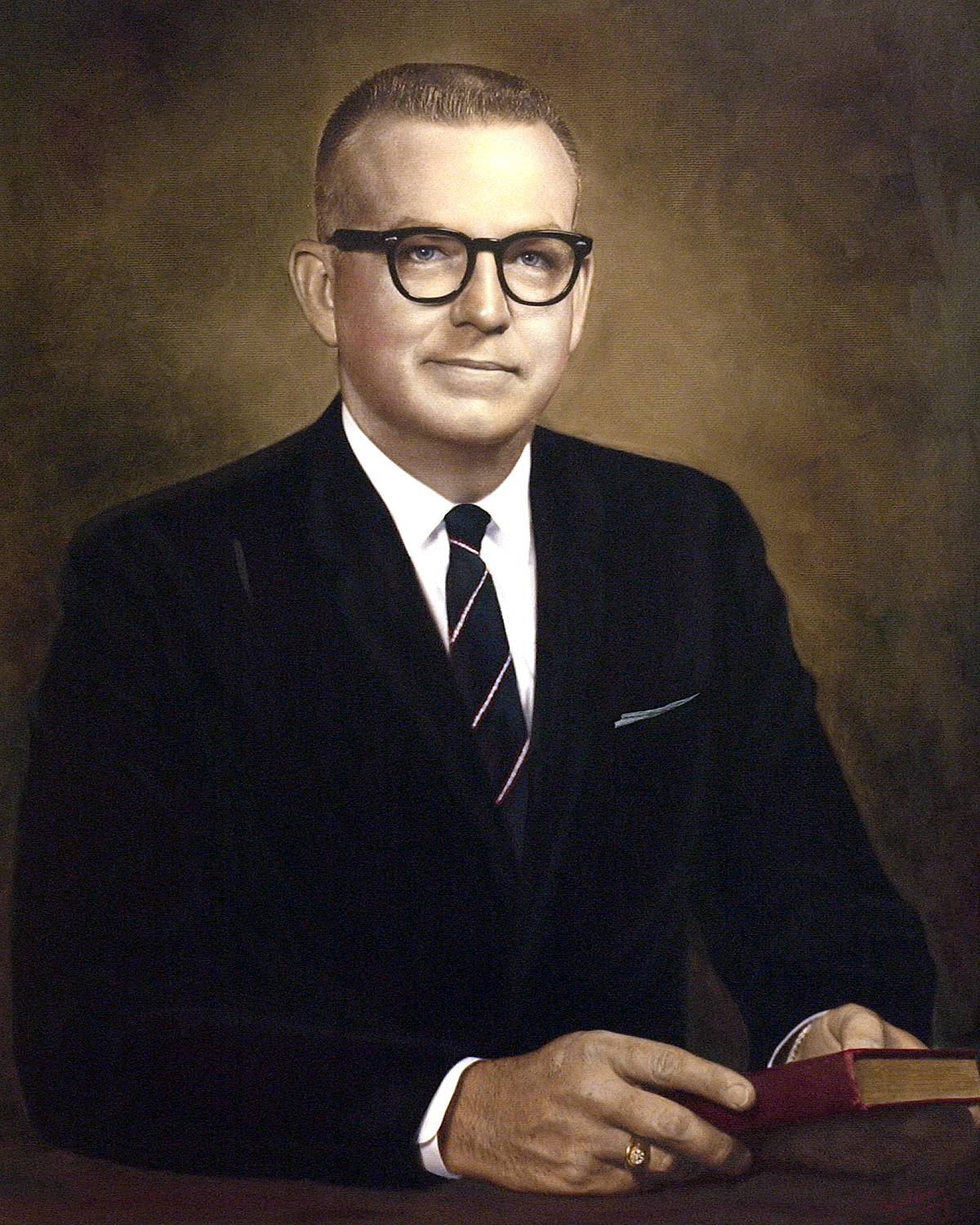 A portrait of TXST President James H. McCrocklin. A middle-aged man wearing black spectacles and a dark suit with a striped tie, President McCrocklin appears very professional. 