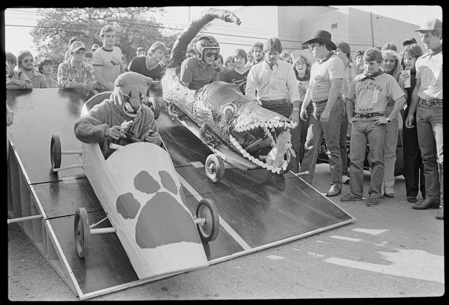 Two students descending the race ramp in their soap box cars with a crowd around them.