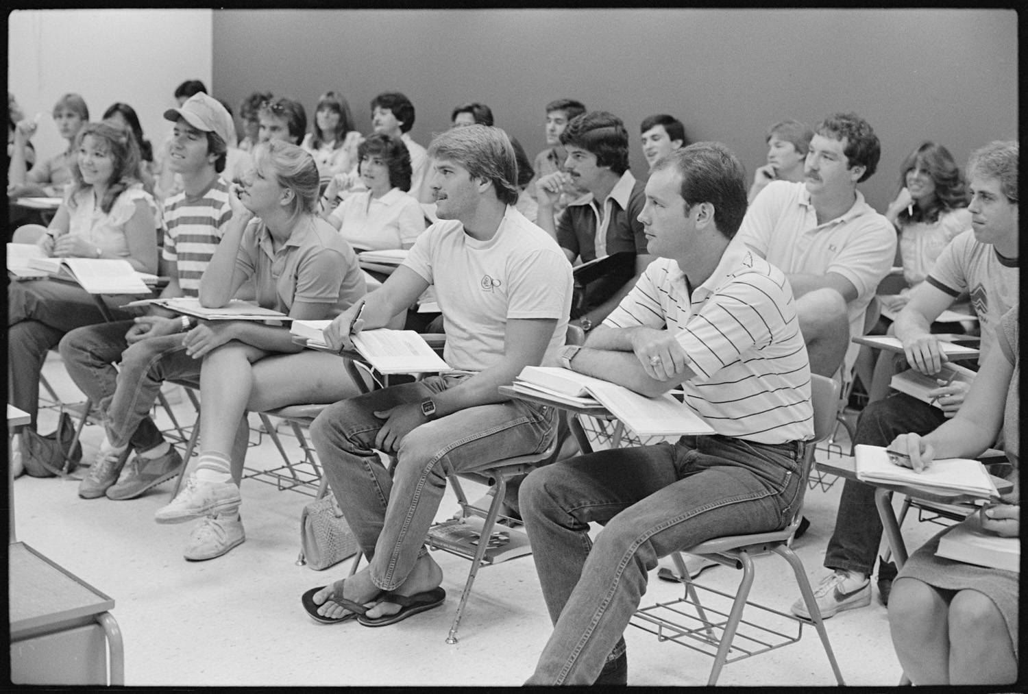 A black-and-white photo of a large mixed-gender group of students in a business class looking at the professor as the class is being conducted. 