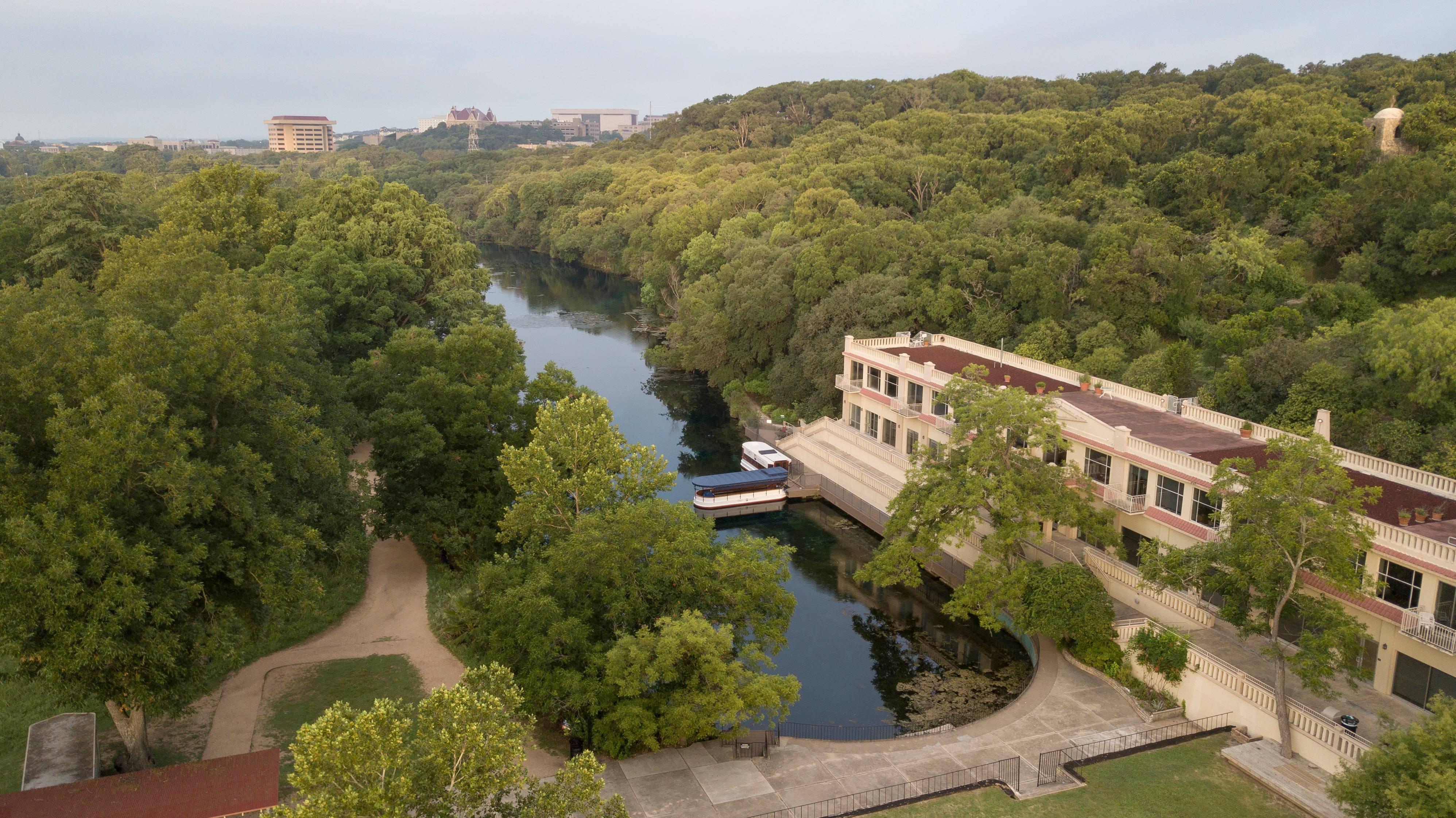 An aerial view of the Meadows Center with Spring Lake and the surrounding hills. A number of San Marcos Campus buildings can be seen in the background, including Old Main, J.C. Kellam, Alkek and several others. 