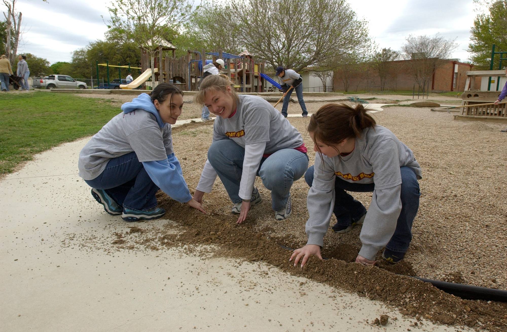 Three female volunteers packing soil into the ground. 