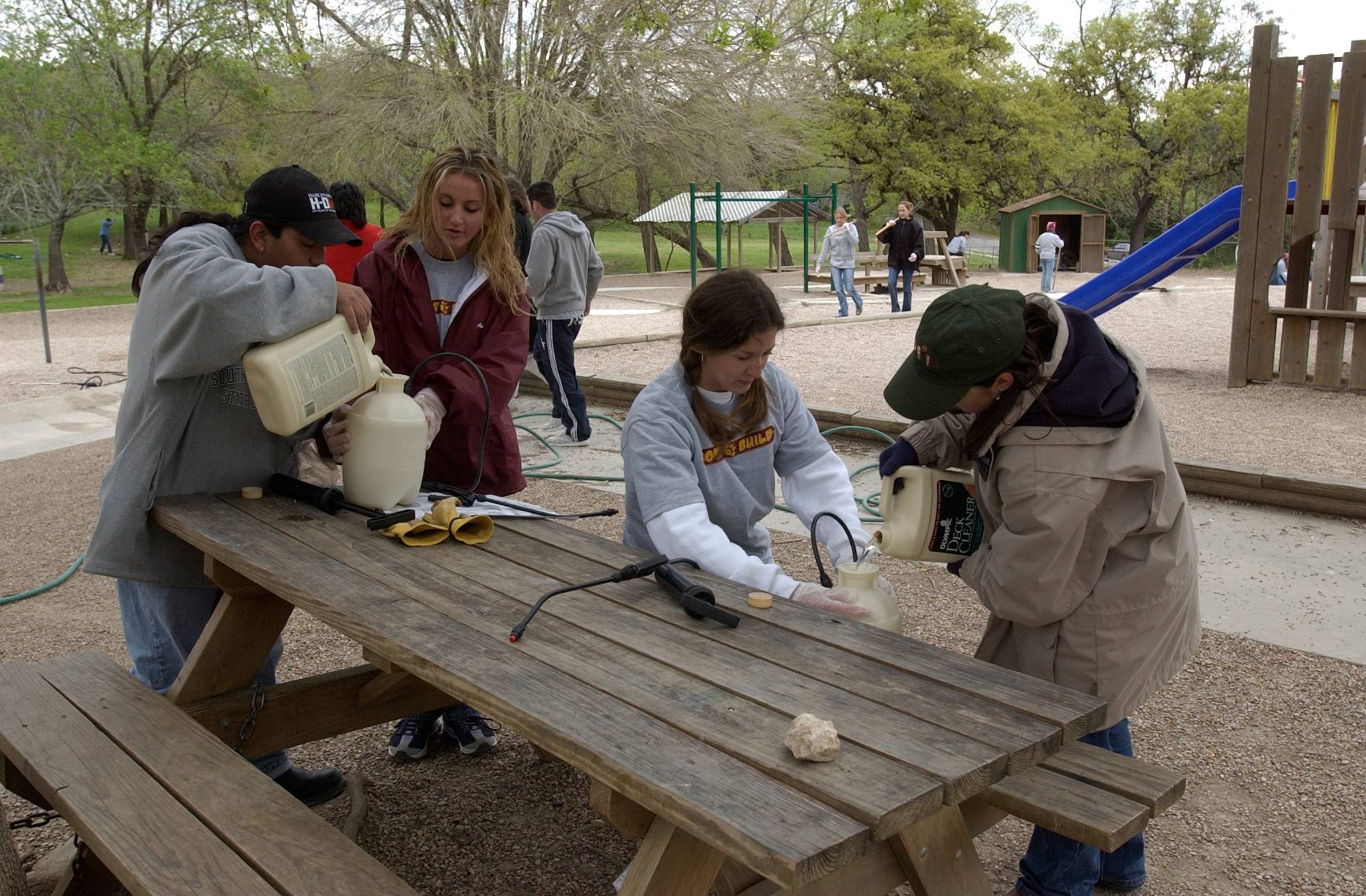 Two pairs of volunteers pouring deck cleaning solution into containers. 