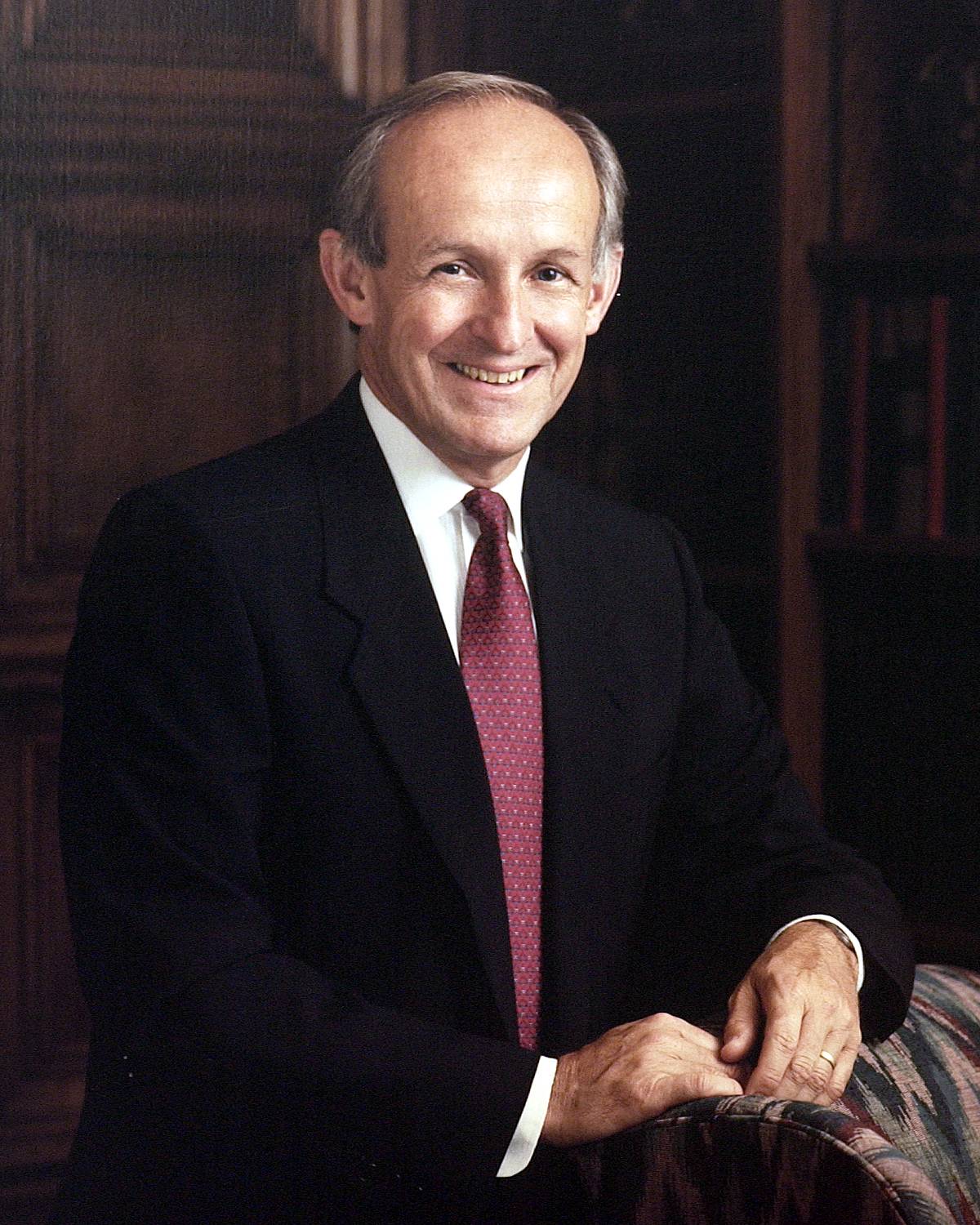 A photo of former TXST President Jerome H. Supple, smiling pleasantly. He is dressed in a dark suit, paired with a white shirt and a maroon tie.