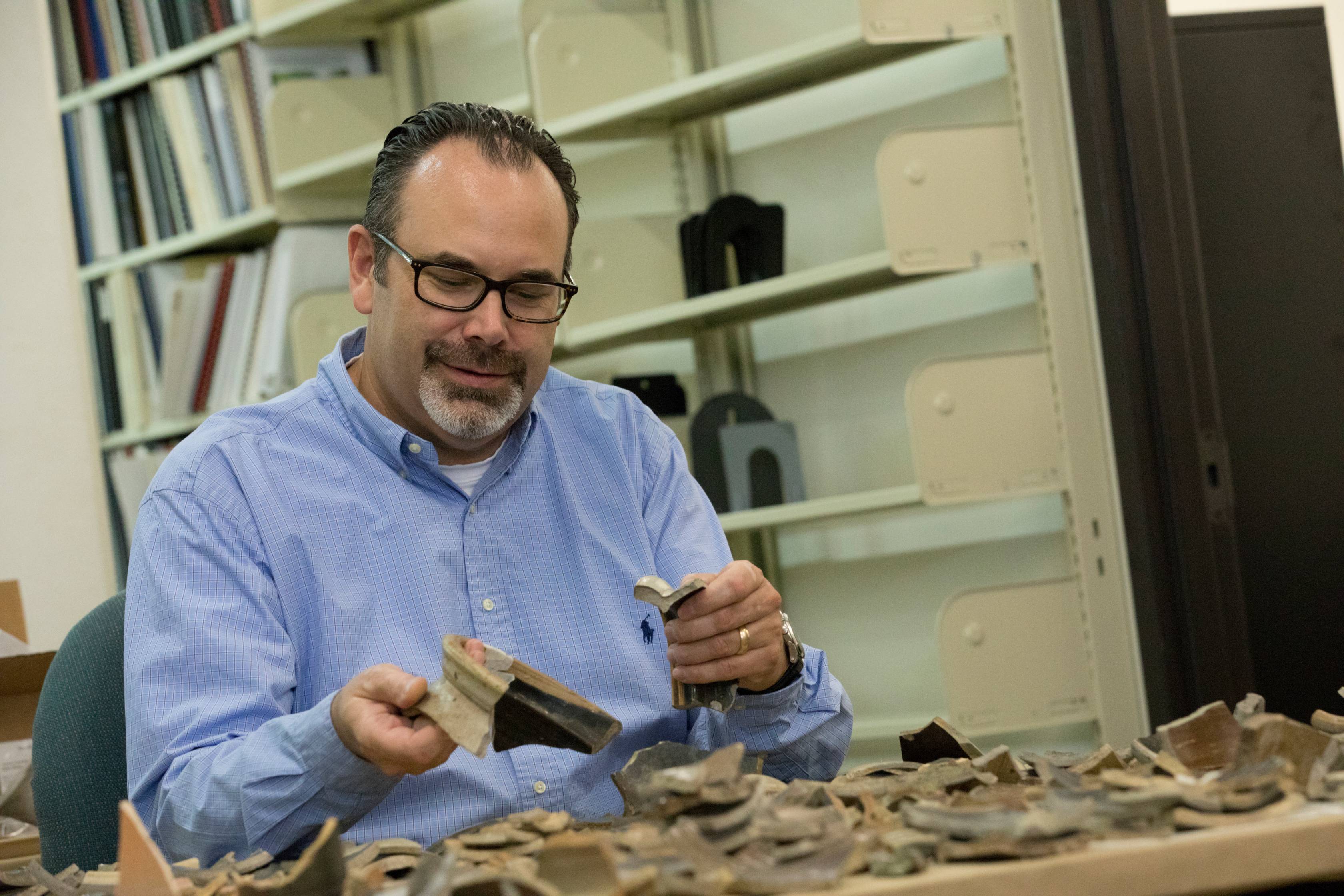 A professor sorting through pieces of pottery. 