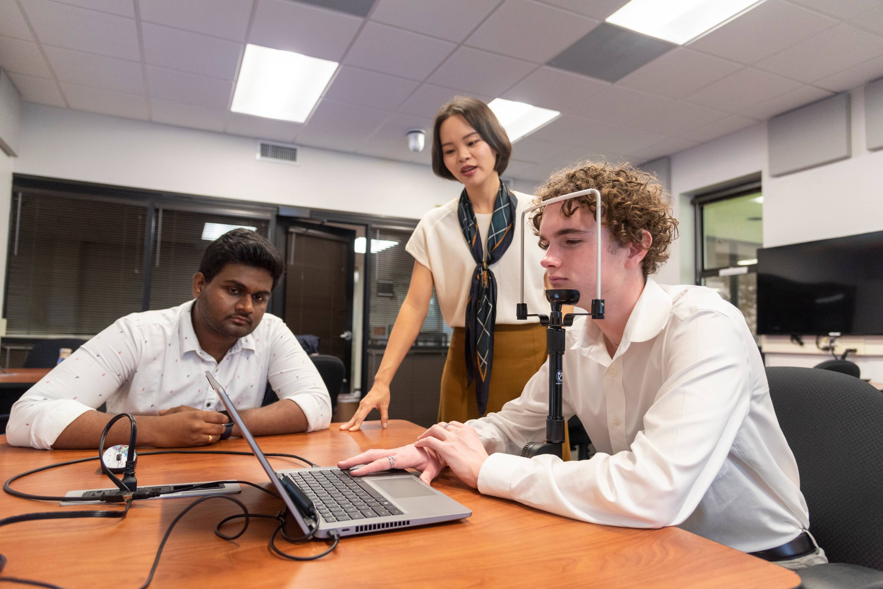 Three TXST students work at a lab table with unique eye-movement technology to capture data for analysis. 