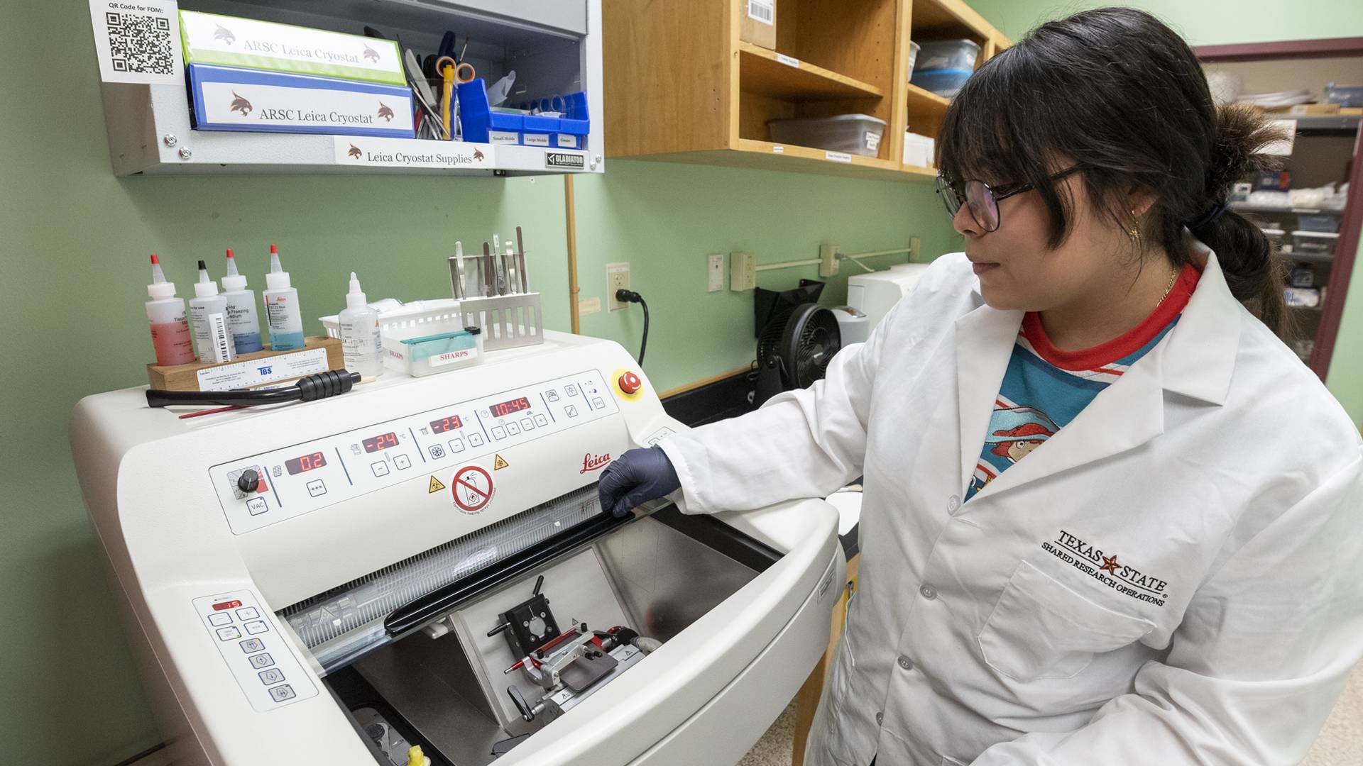 Woman looking into science equipment wearing a labcoat