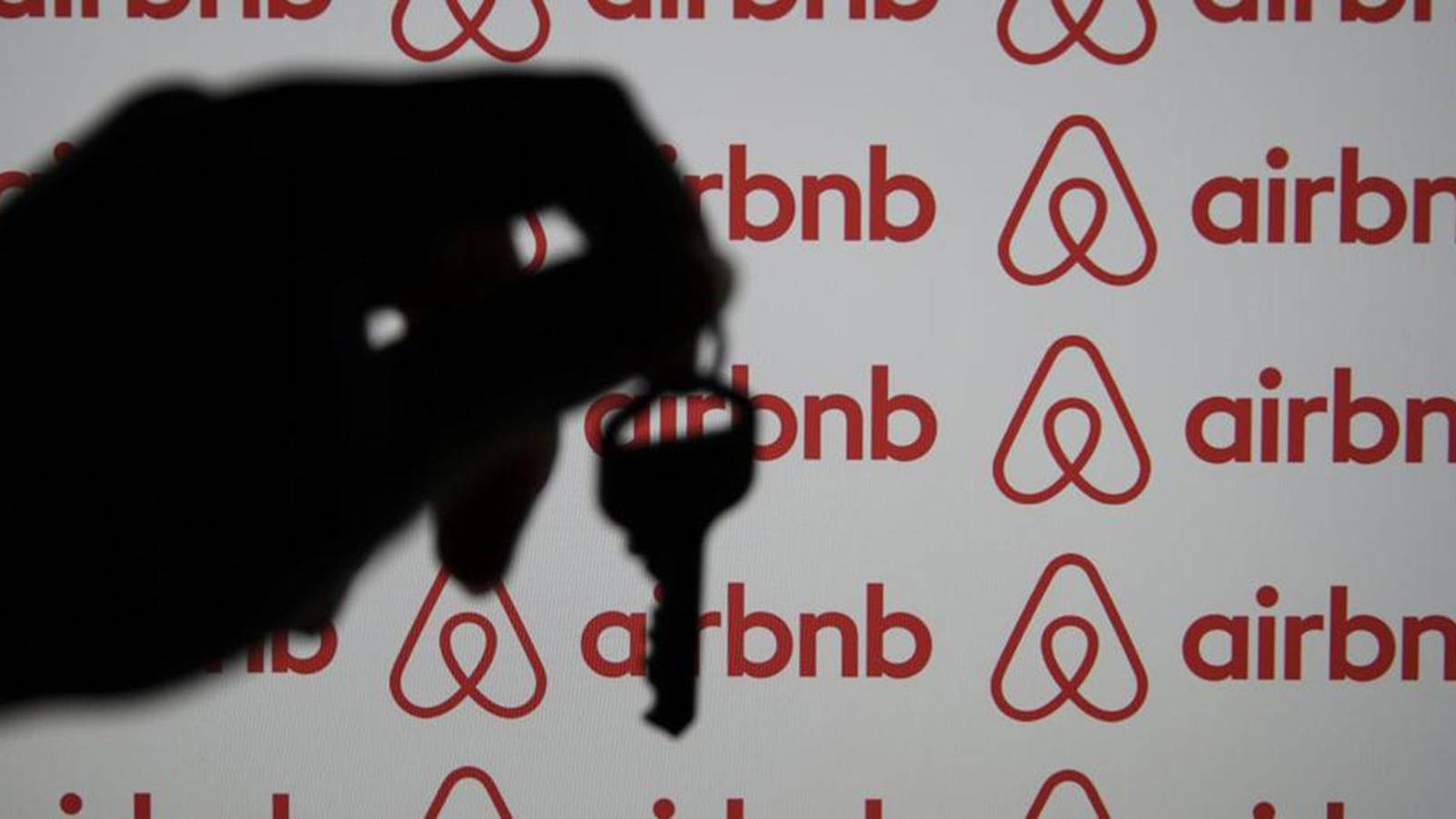 Silhouetted hand holding key over a background with Airbnb logo