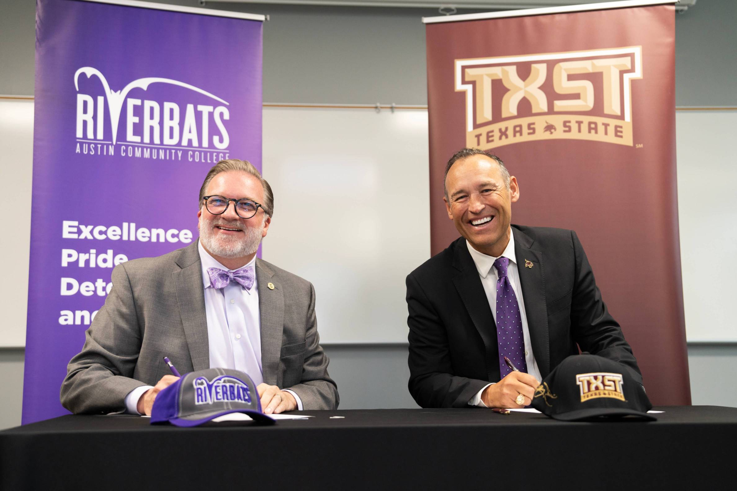 ACC Chancellor Russell Lowery-Hart and TXST President Kelly Damphousse smile in front of their respective school banners at the Bats to Cats signing event.