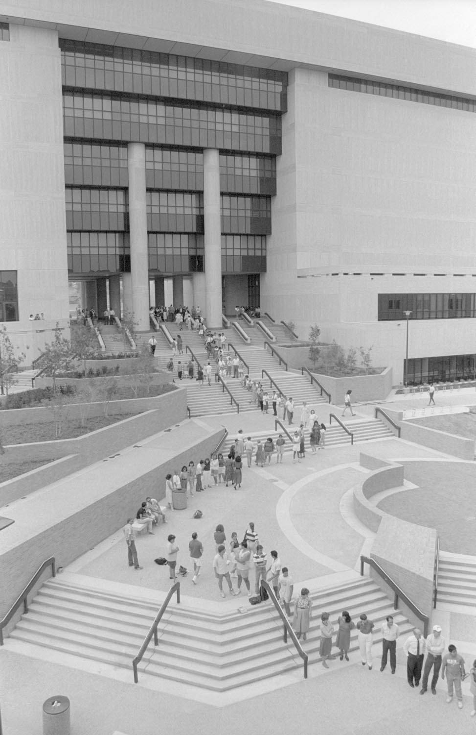 Black and white photo taken from a few stories up of a line of students flowing out of a building and snaking down steps and sidewalk.