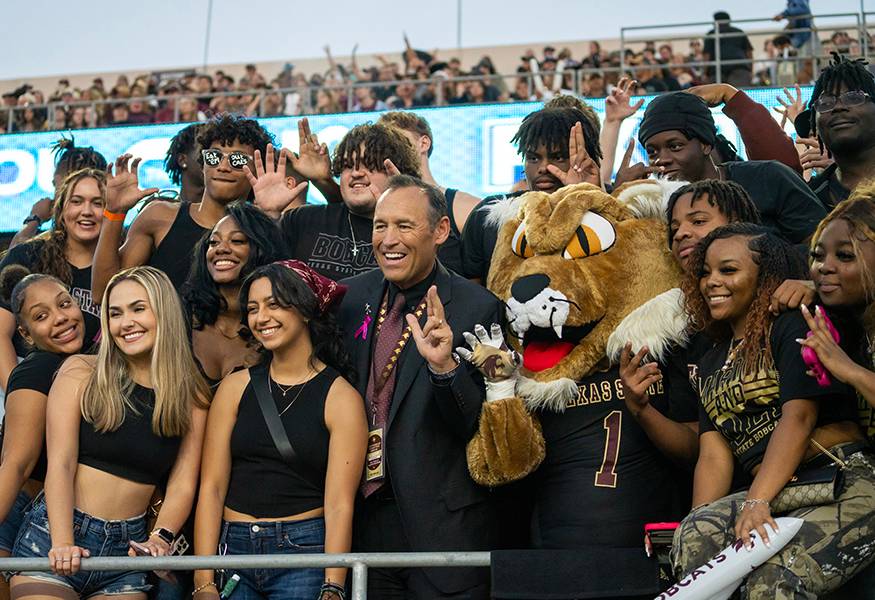 group of students posing with TXST president and Boko at a Bobcat sports event
