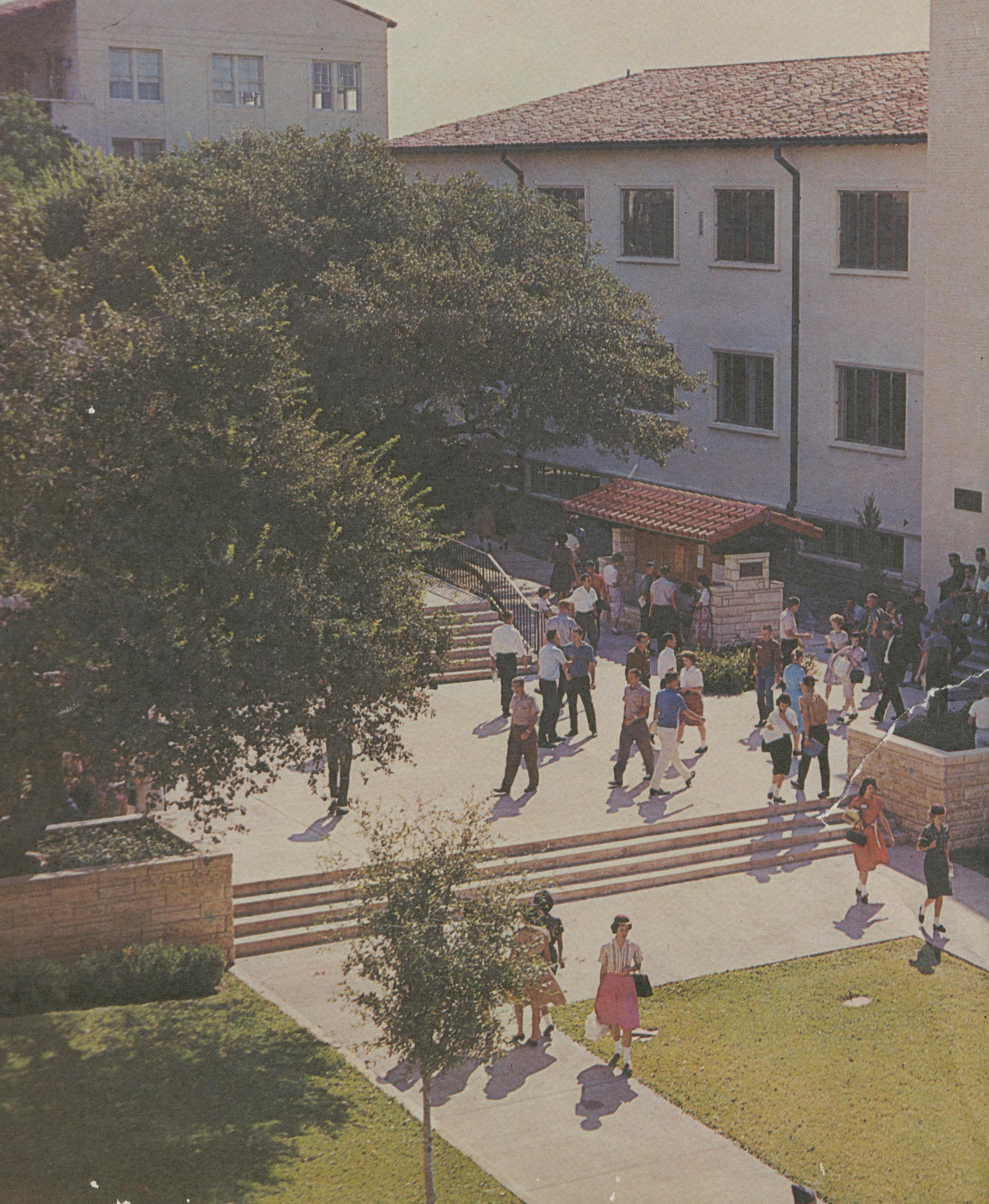 Colorized shot of 1960s campus, taken from a second-story view. Below, young people in brightly colored outfits are milling about or on their way to class.