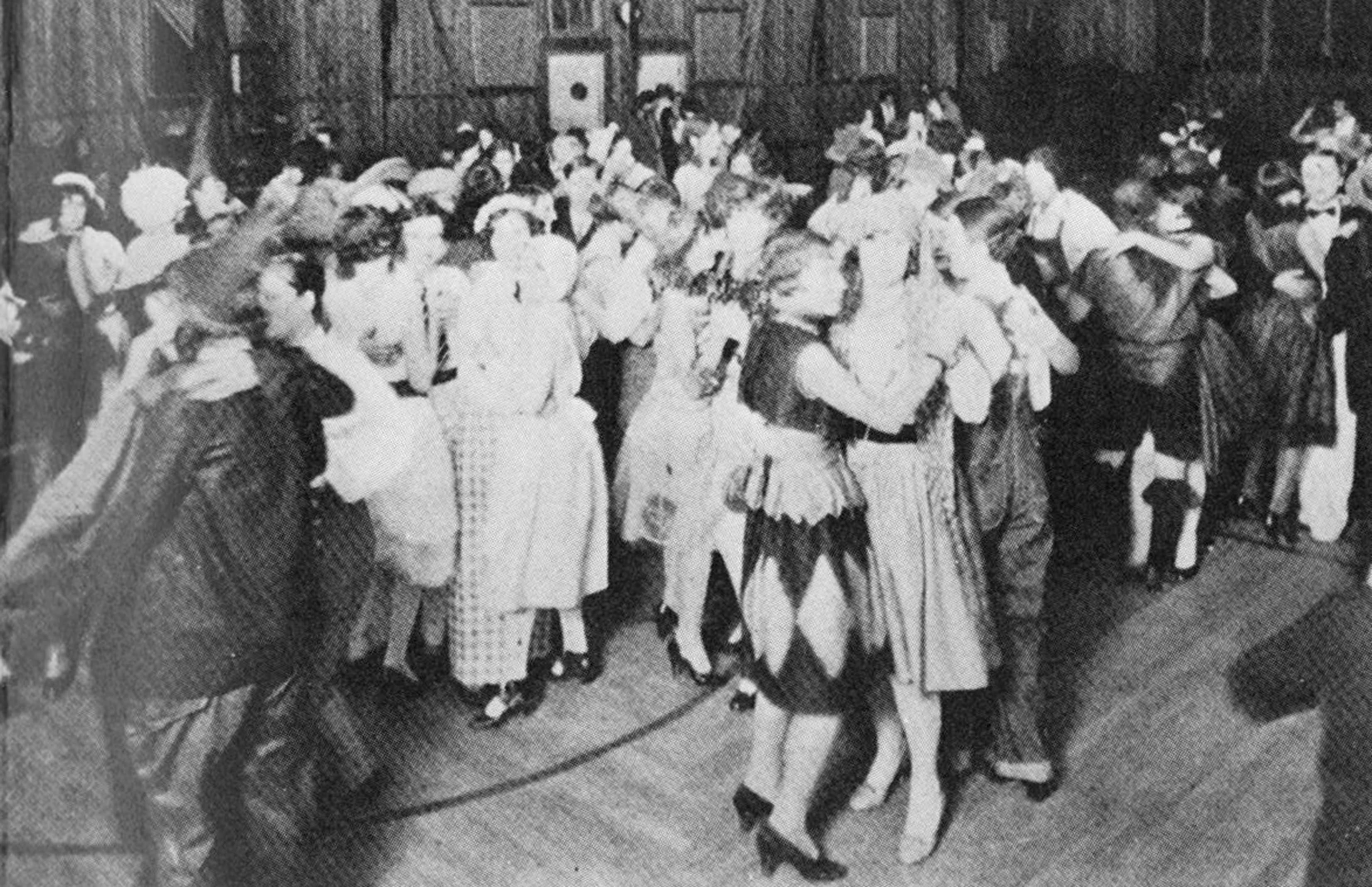 Aged black and white photo of a campus dance at the then Southwest Texas State Normal College, held in the school's gymnasium. Students are smiling and laughing as they dance the night away.