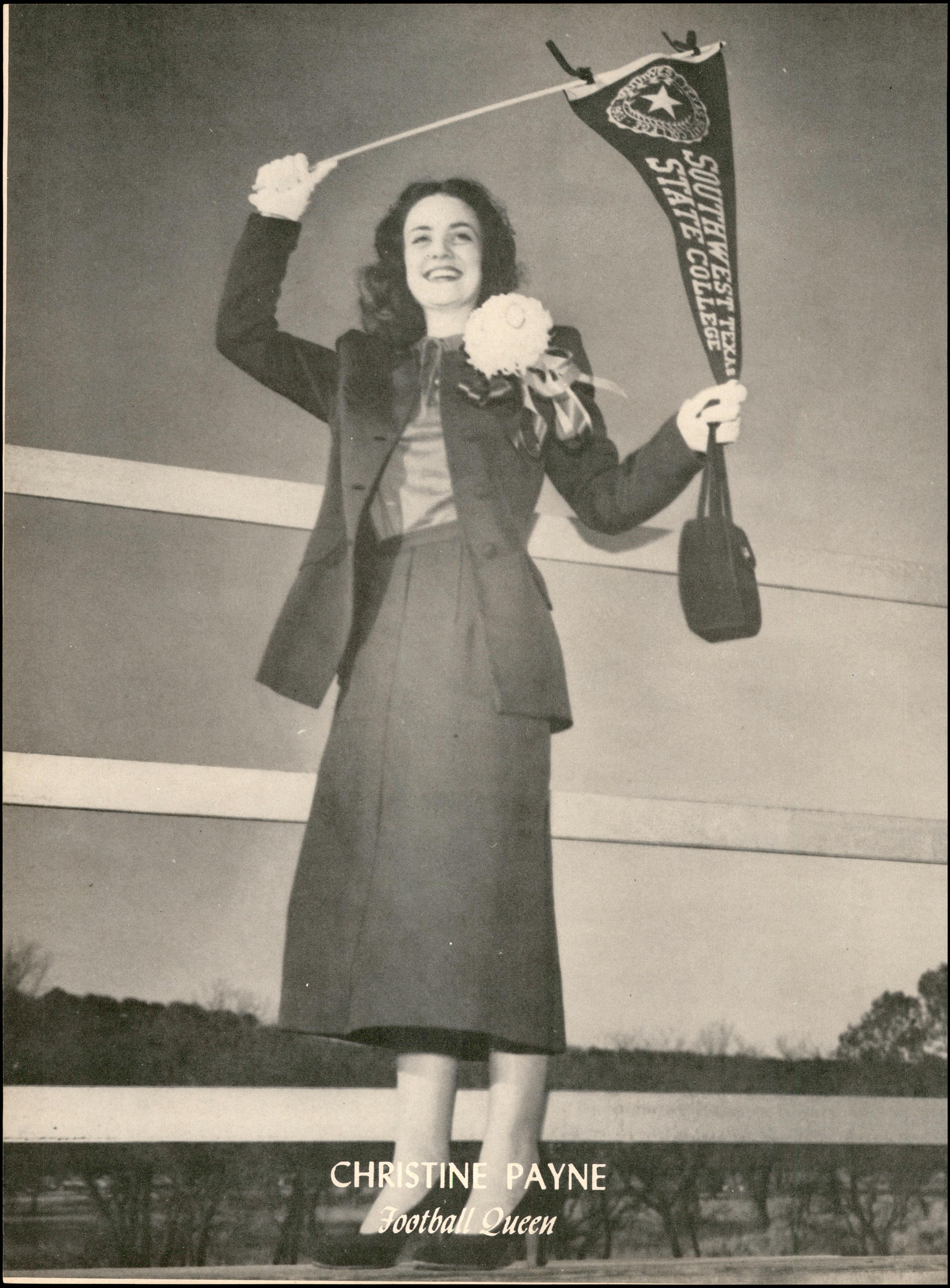 A clipping from 1951, a pretty young lady is pictured wearing a dark skirt suit with a large white flower corsage pinned to her jacket, she smiles exuberantly and stands outside, waving a pennant reading 'Southwest Texas State College' above her head. She holds the tip of the flag to ensure it's legible for the camera. The photo is captioned 'Christine Payne, Football Queen.' 