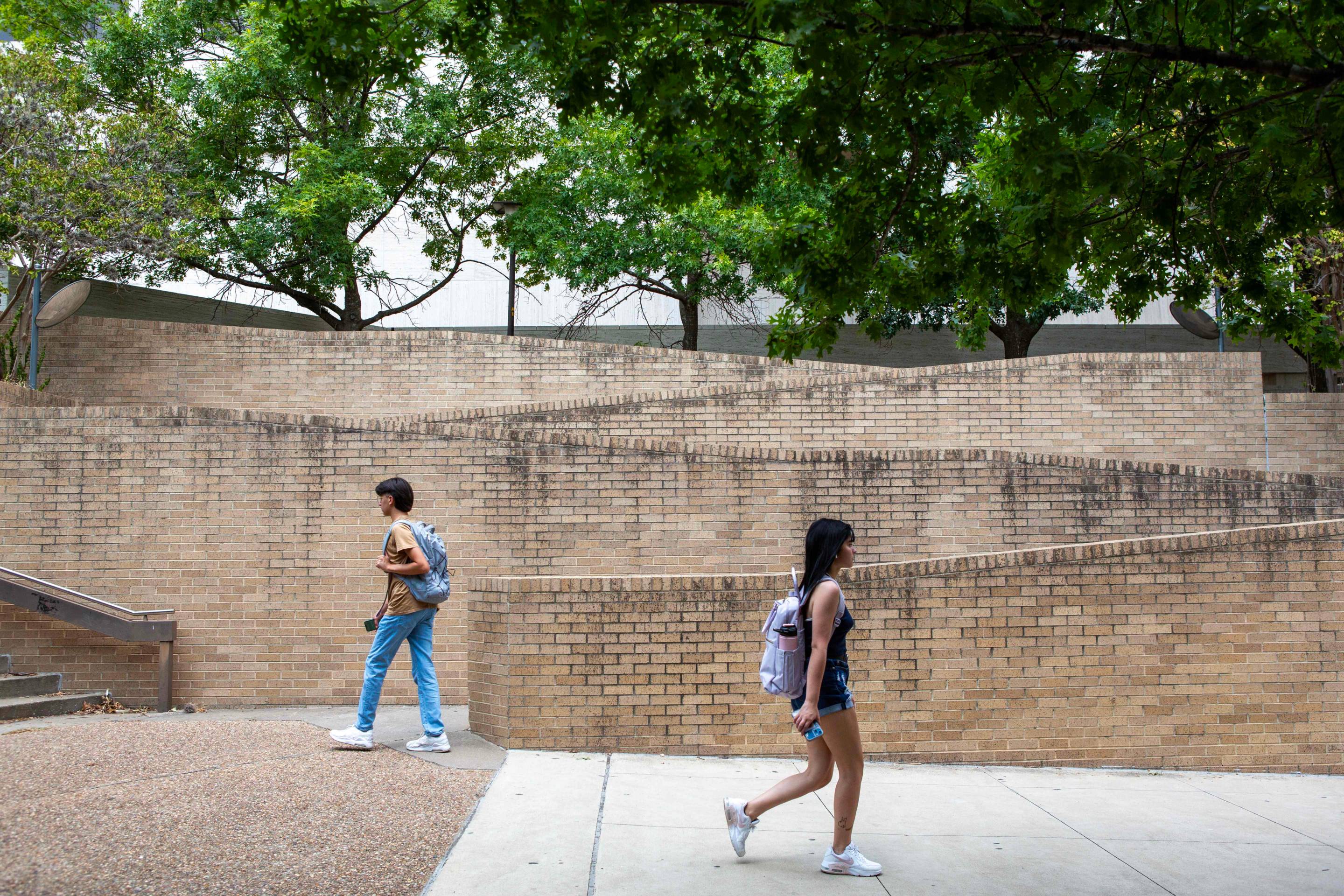 Two young folks with backpacks walk in opposite directions on a brick pathway.