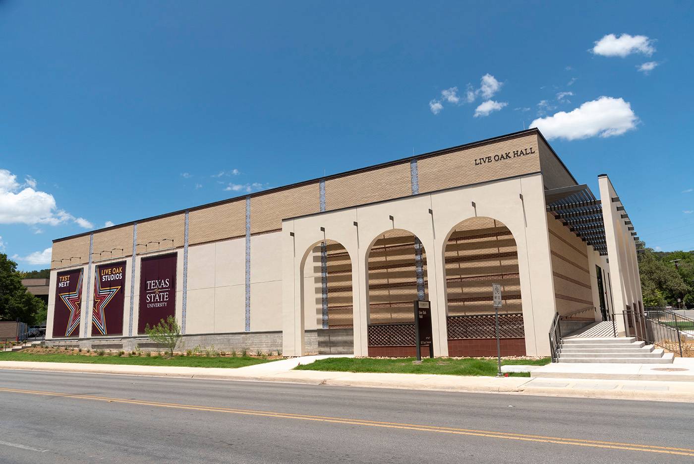 Large, square building with rounded arches. The building is tan in color and has large, maroon banners on the left-hand side. The upper right corner says "Live Oak Hall".