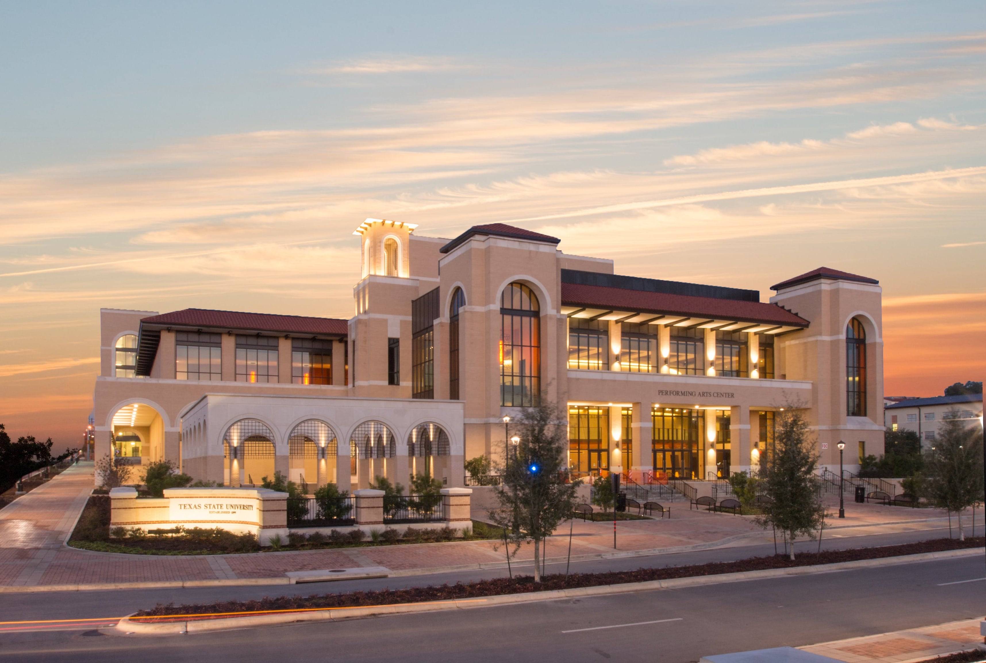 Shot of an impressive building lit up with exterior lights. The backdrop of a sunset is behind it.