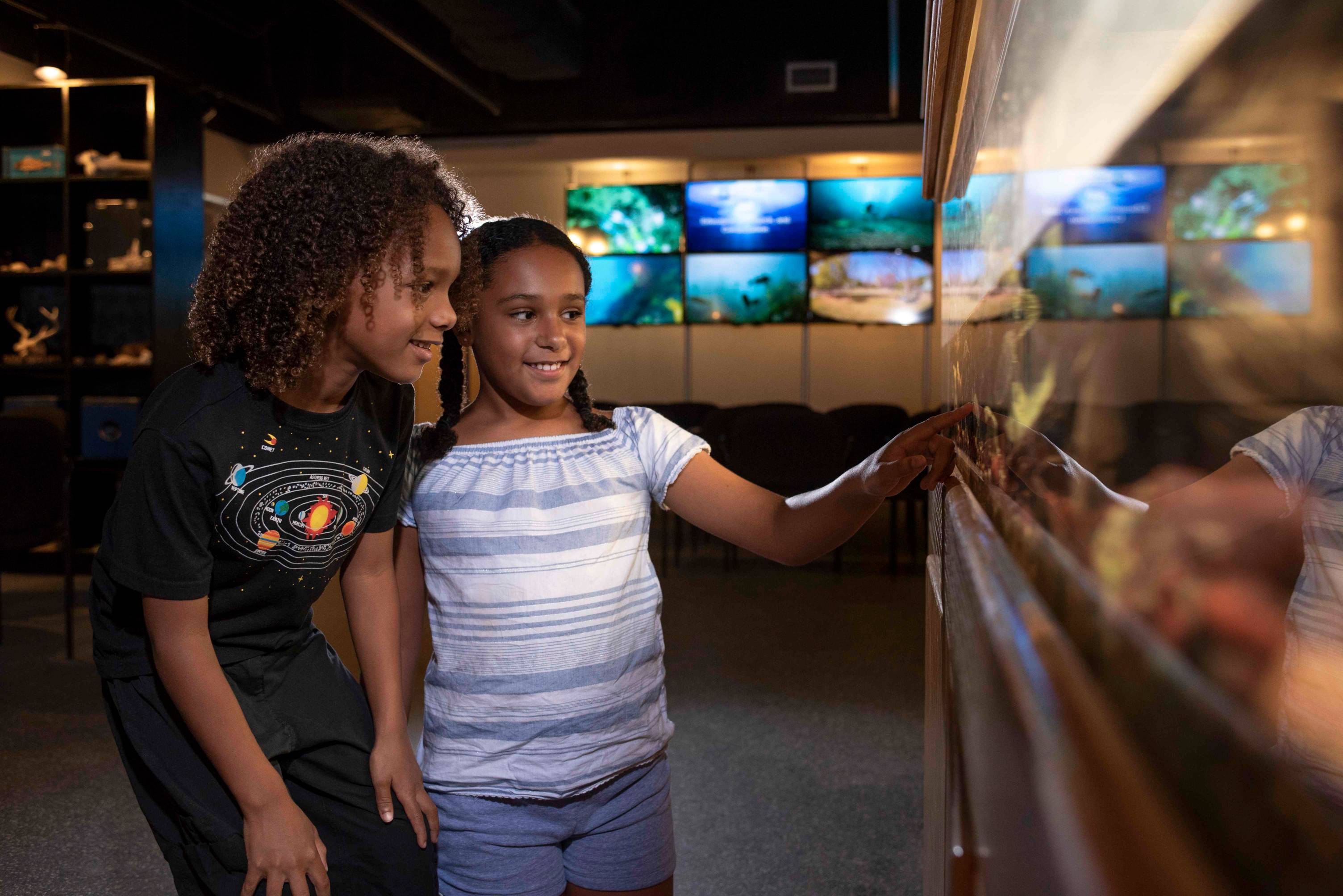 Close up shot of two young girls smiling and looking at an aquarium.