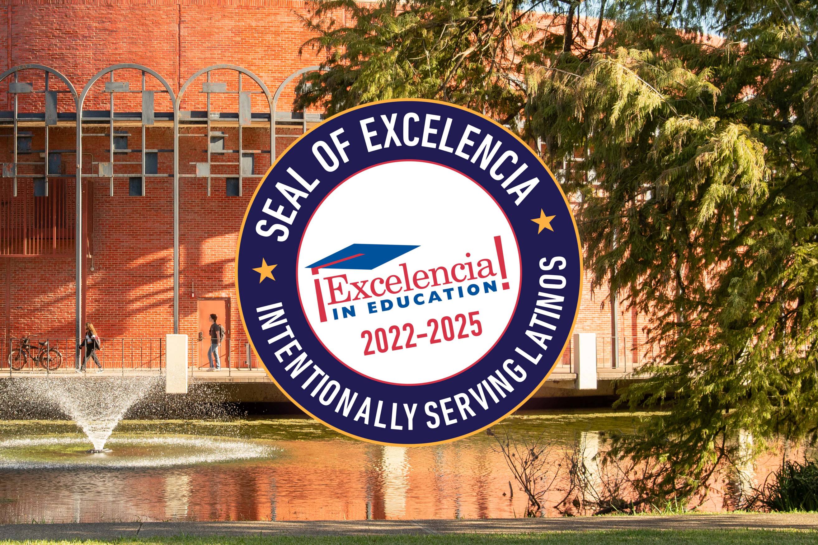 A blue, circular seal is superimposed on top of a lanadscape scene. The seal says  "Seal of Excelencia -- Intentionally Serving Latinos -- Excelencia in Education 2022-2025". The background scene shows a pond with a fountain in front of a building on a sunny day.