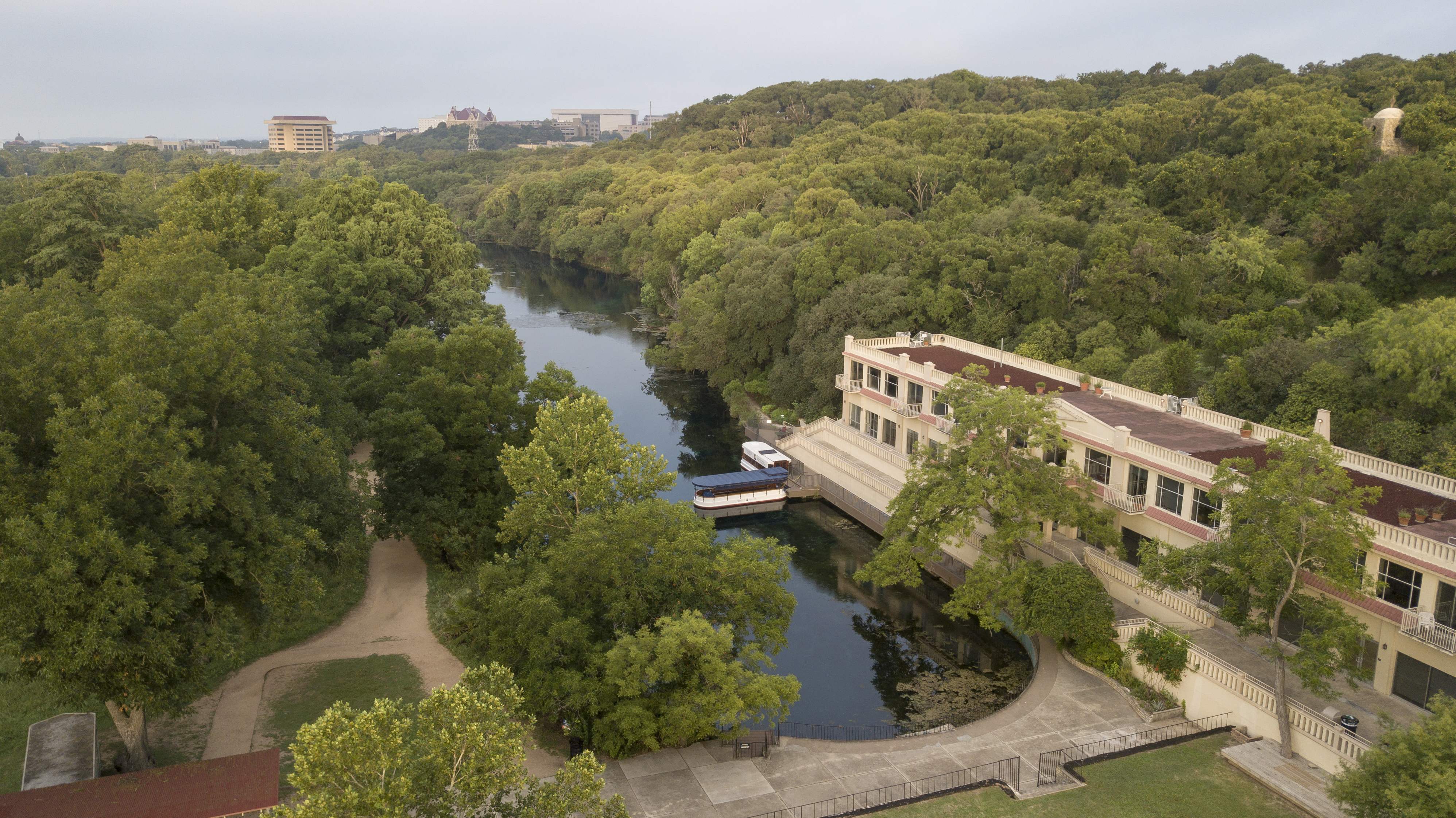 Aerial image of Spring Lake flanked on either side by lush trees. To the right, a large, red-roofed building sits close to the banks. A covered boat can be seen docked near the building.