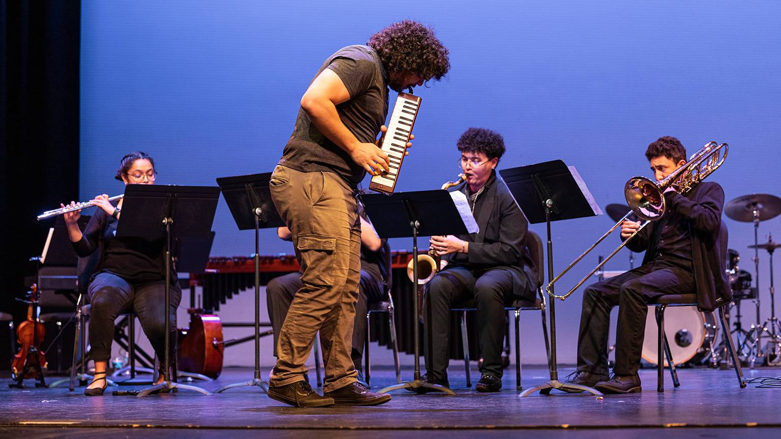 Jay Nava, middle, plays the melodica on stage in front of an ensemble during his hip-hop opera.