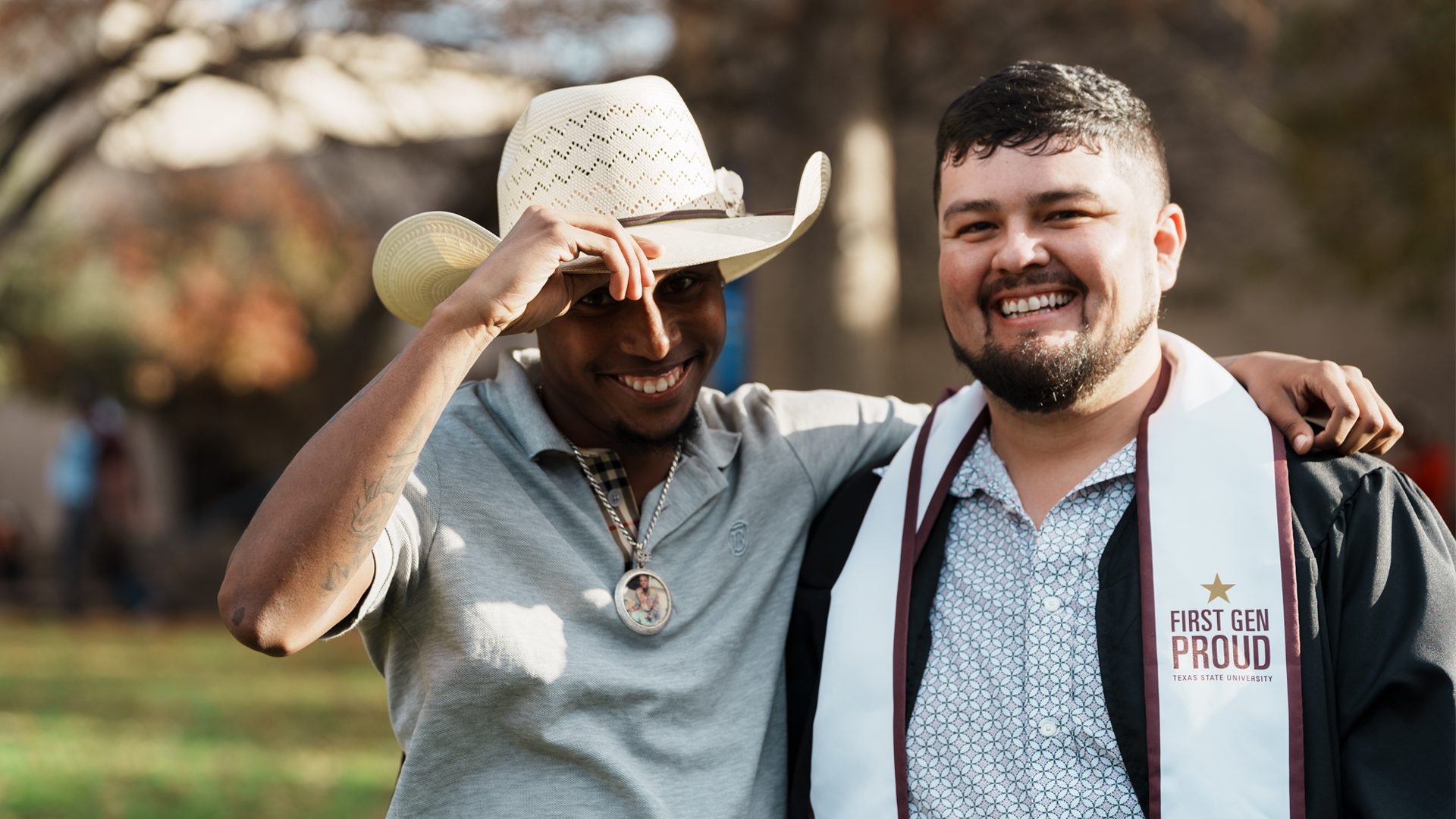 two men smiling next to each other, one is wearing graduation attire