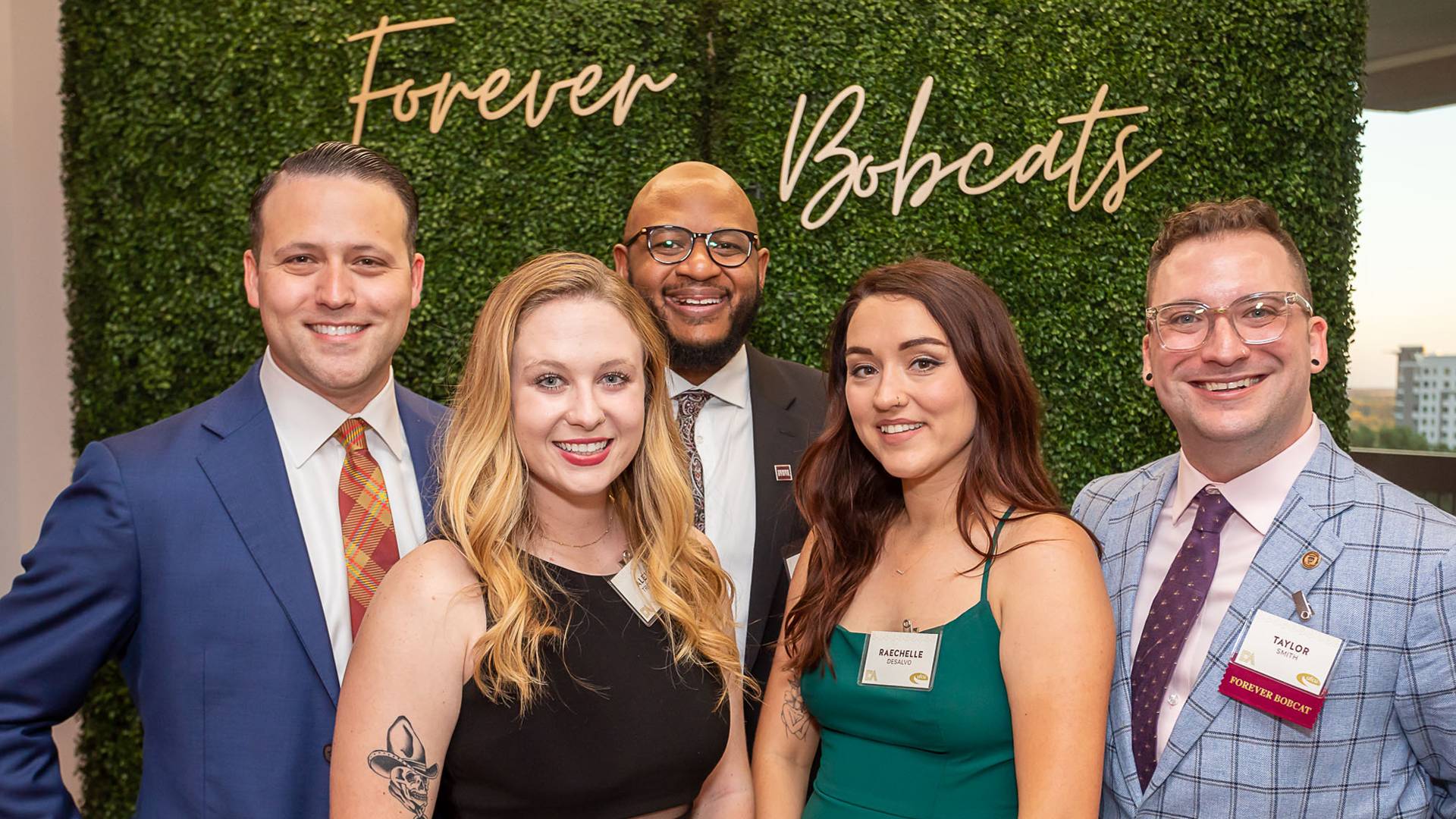 group photo of five people in formal wear in front of a forever bobcat sign