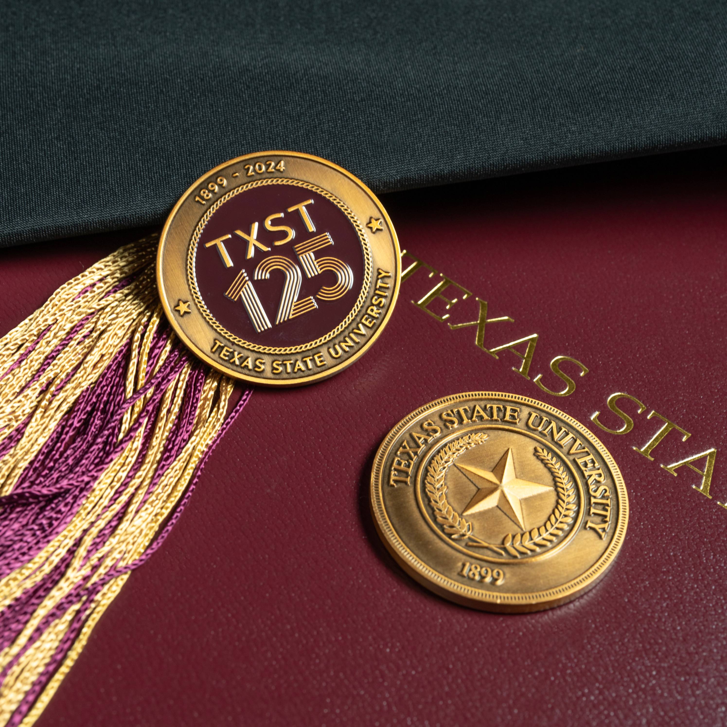 two challenge coins on maroon background with a maroon and gold tassel to the side