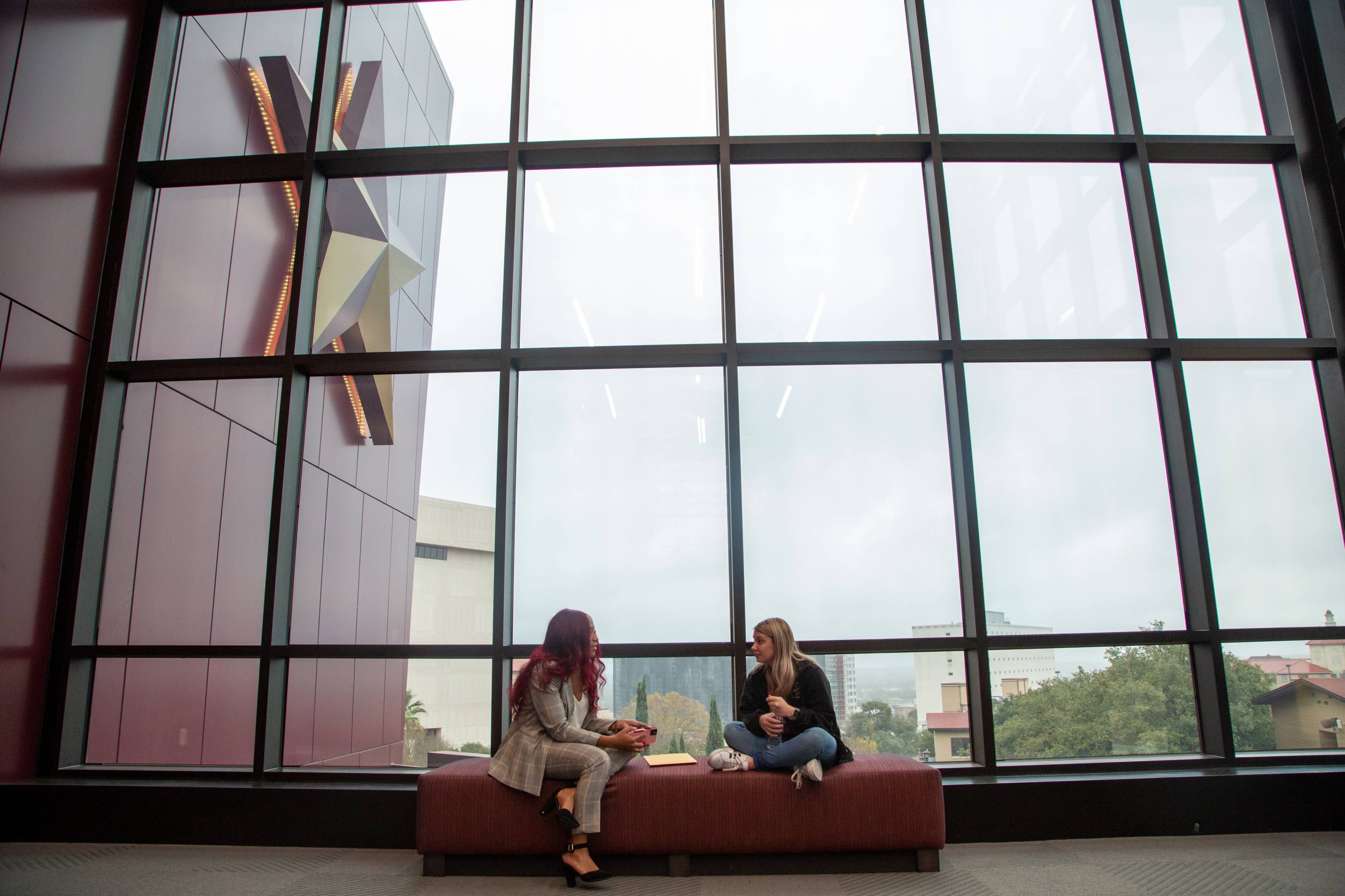 Two students sitting down together in front of a window at the LBJ student center