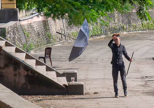 Picture of an umbrella floating in the wind while a  man stands to the right of the umbrella. There is a set of concrete stairs to the left of the umbrella.