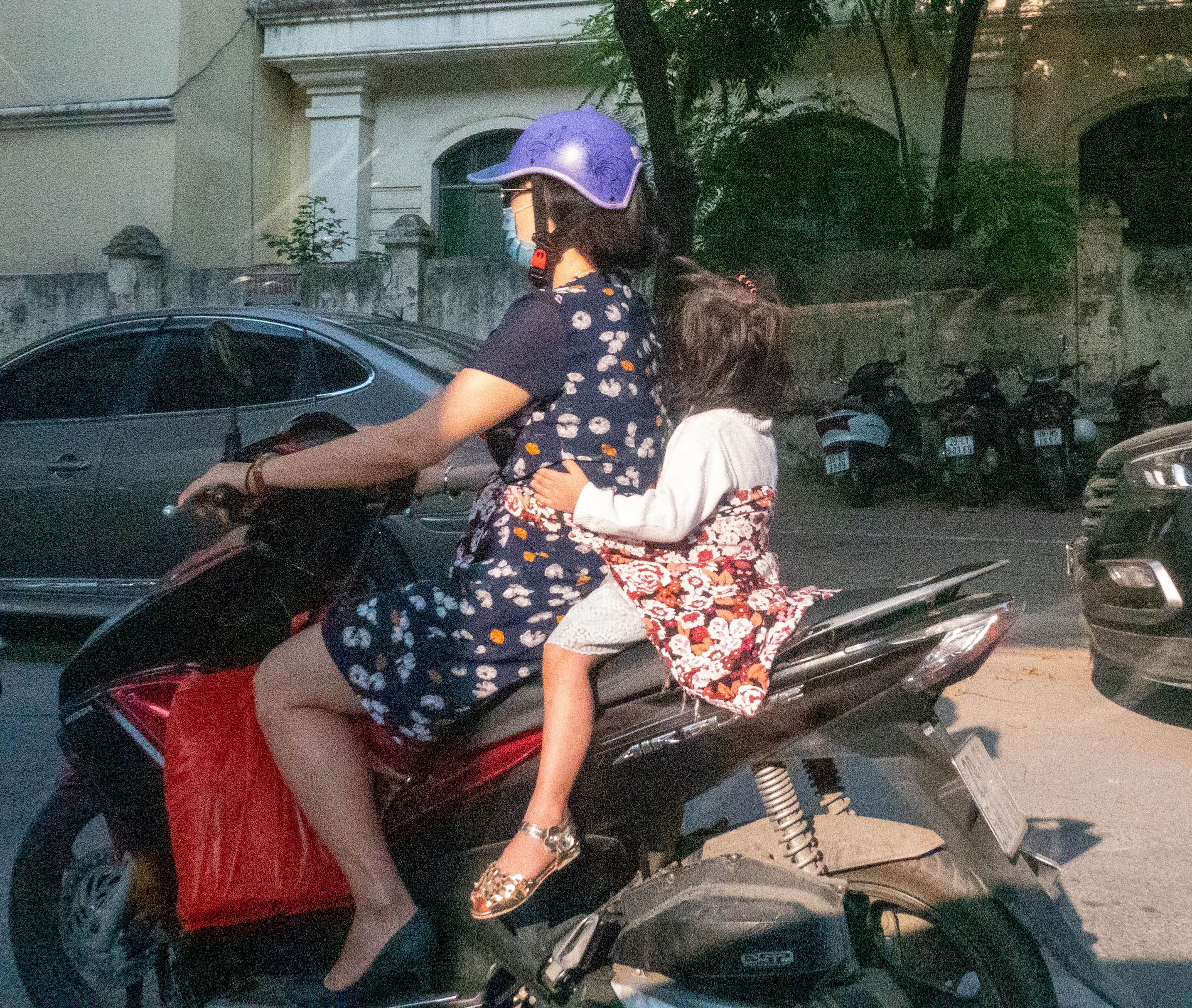 mother and child on motorbike. The toddle behind the mother is holding on to the mom and is tied to the mother with a towel