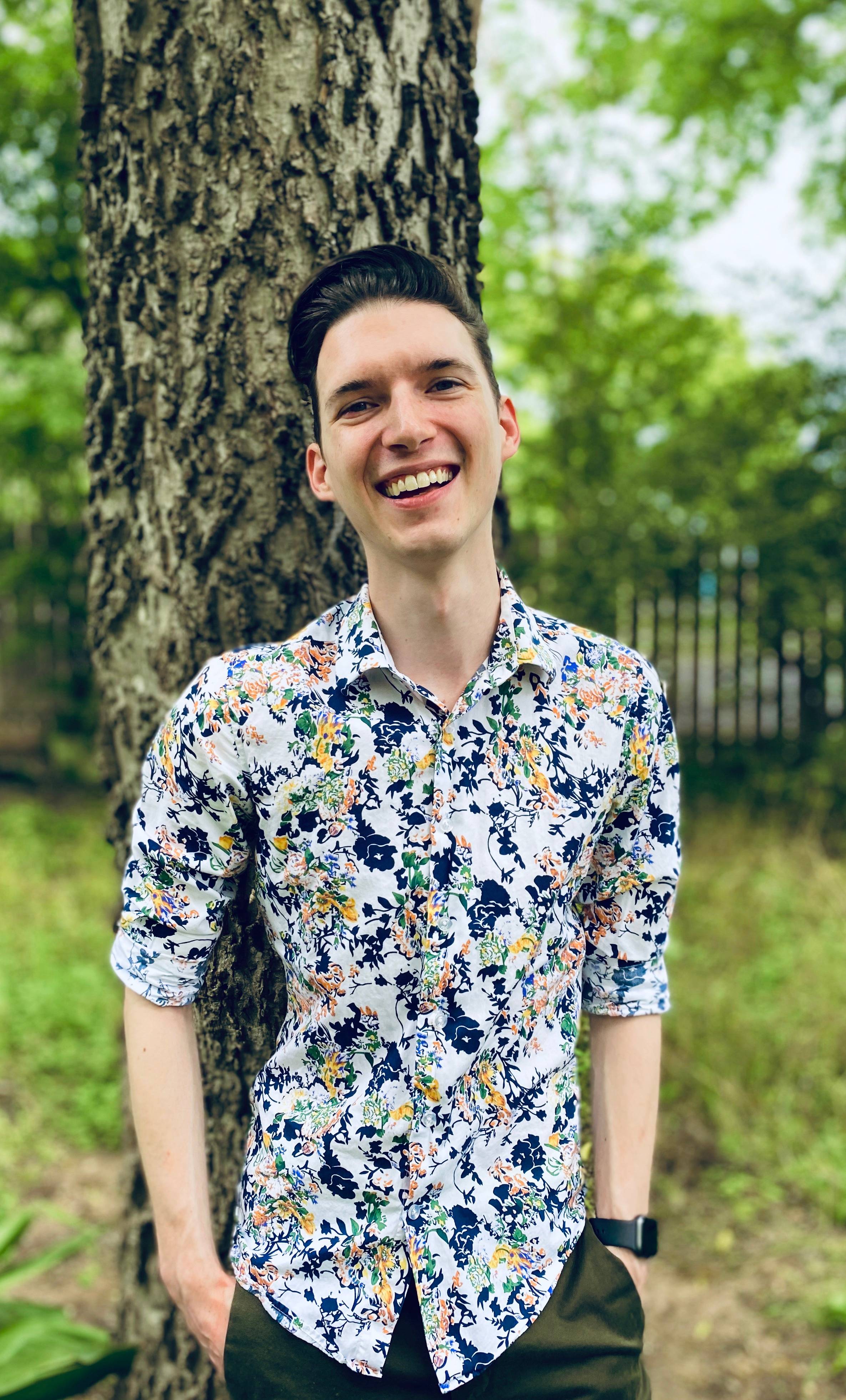 man wearing colorful shirt, leaning against tree