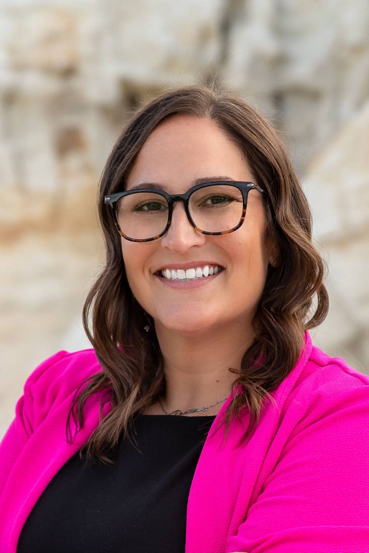 closeup of woman wearing glasses and a pink blazer smiling at camera