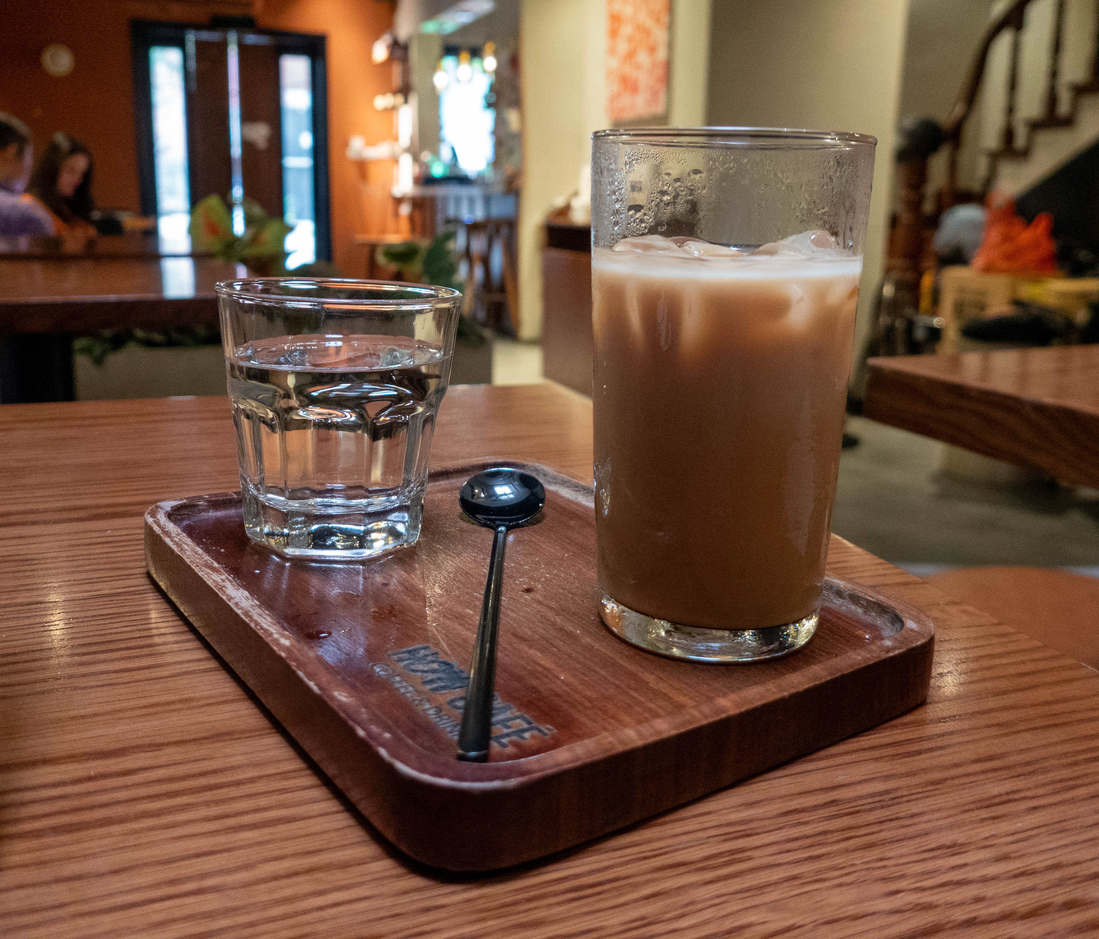 small glass of water on left and tall glass on right with coffee and milk on ice