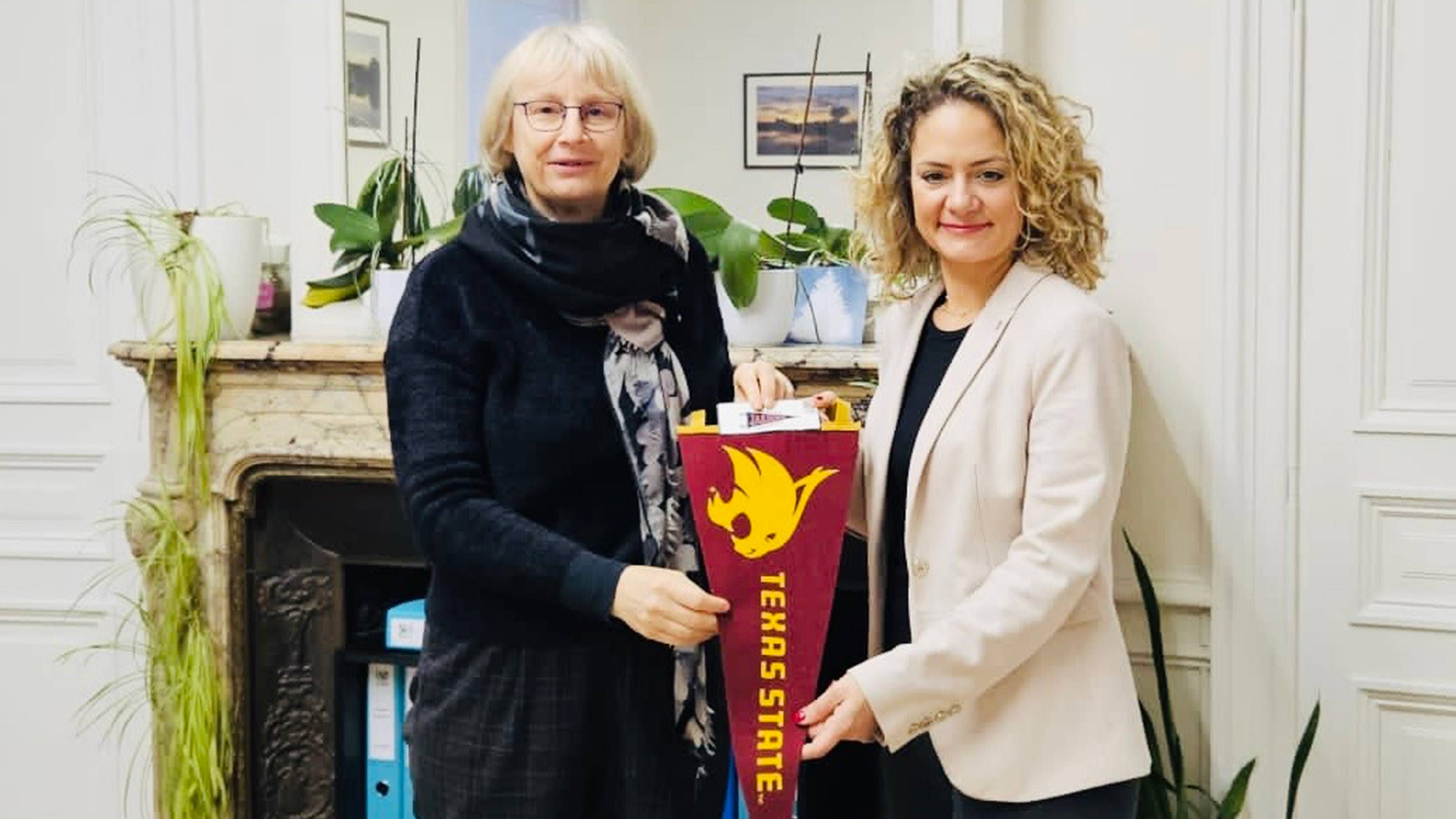 Two women holding a Texas State University pennant