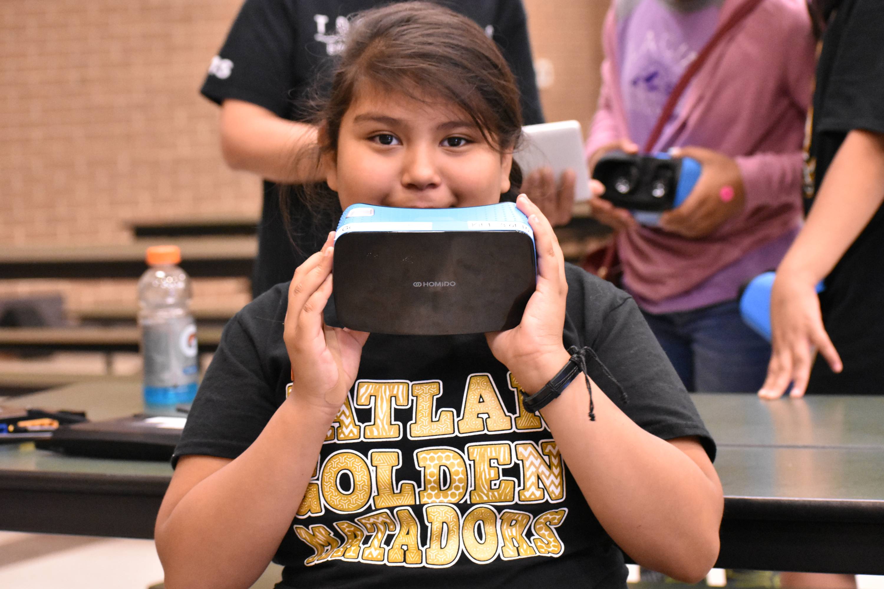 a student poses holding a set of virtual reality goggles over the bottom half of her face, hiding a smile.