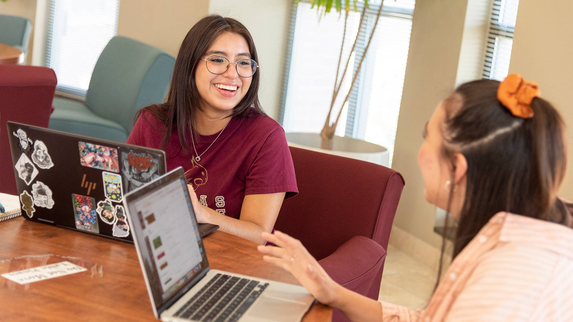 Two students at a table with laptops studying