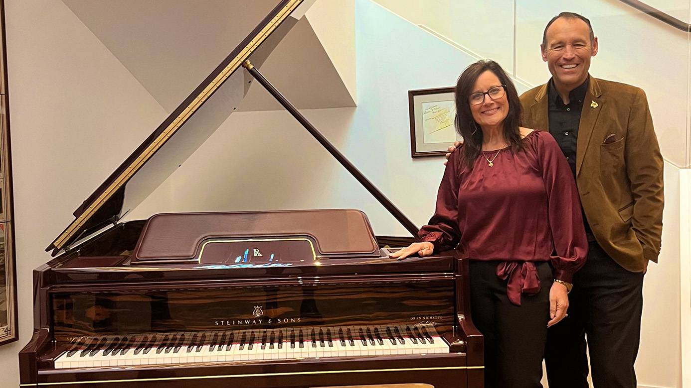 First Lady Damphousse (left) and President Damphousse pose for a photo next to a piano.